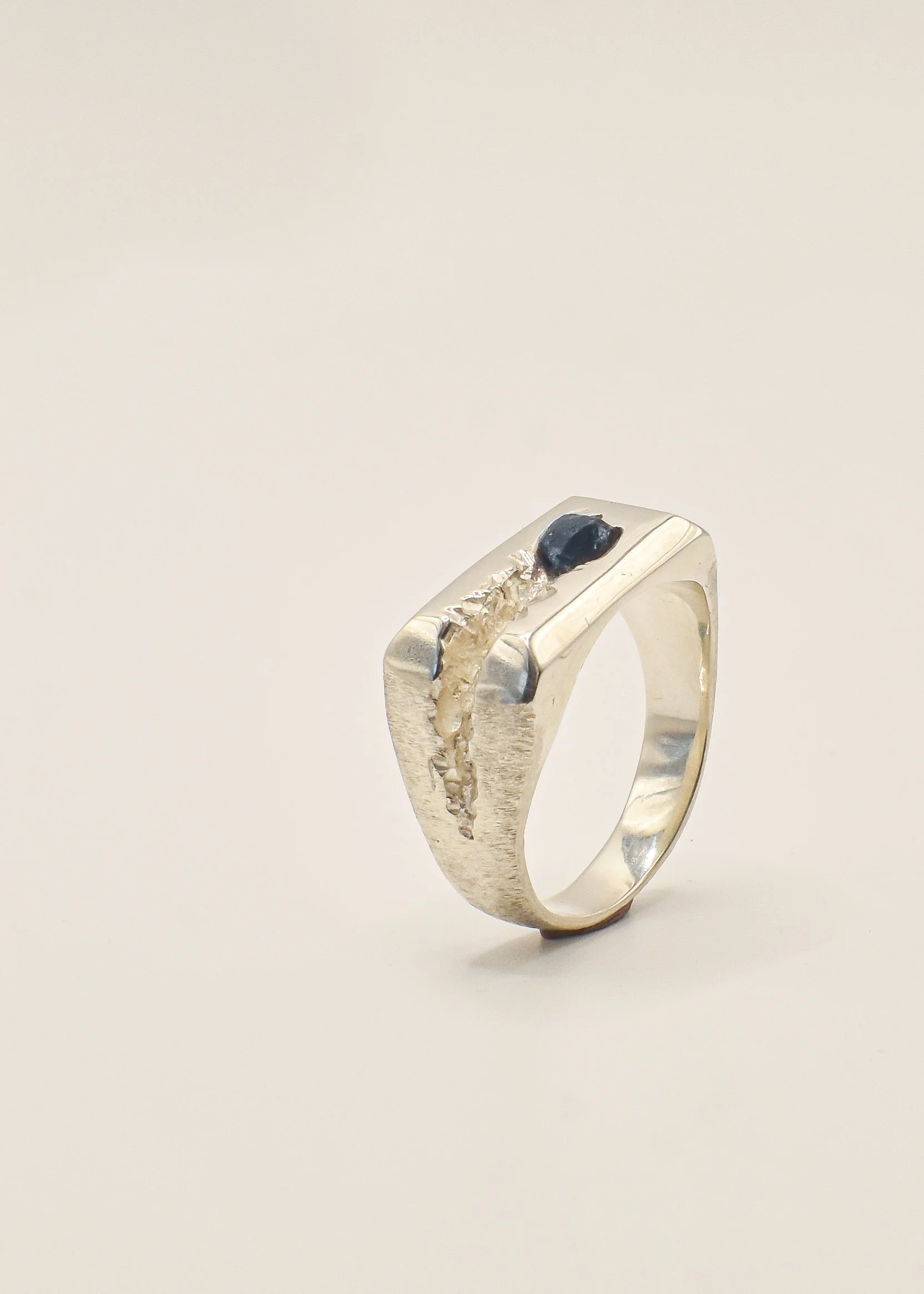 Silver ring with a curved black stone and textured design on a plain beige background.