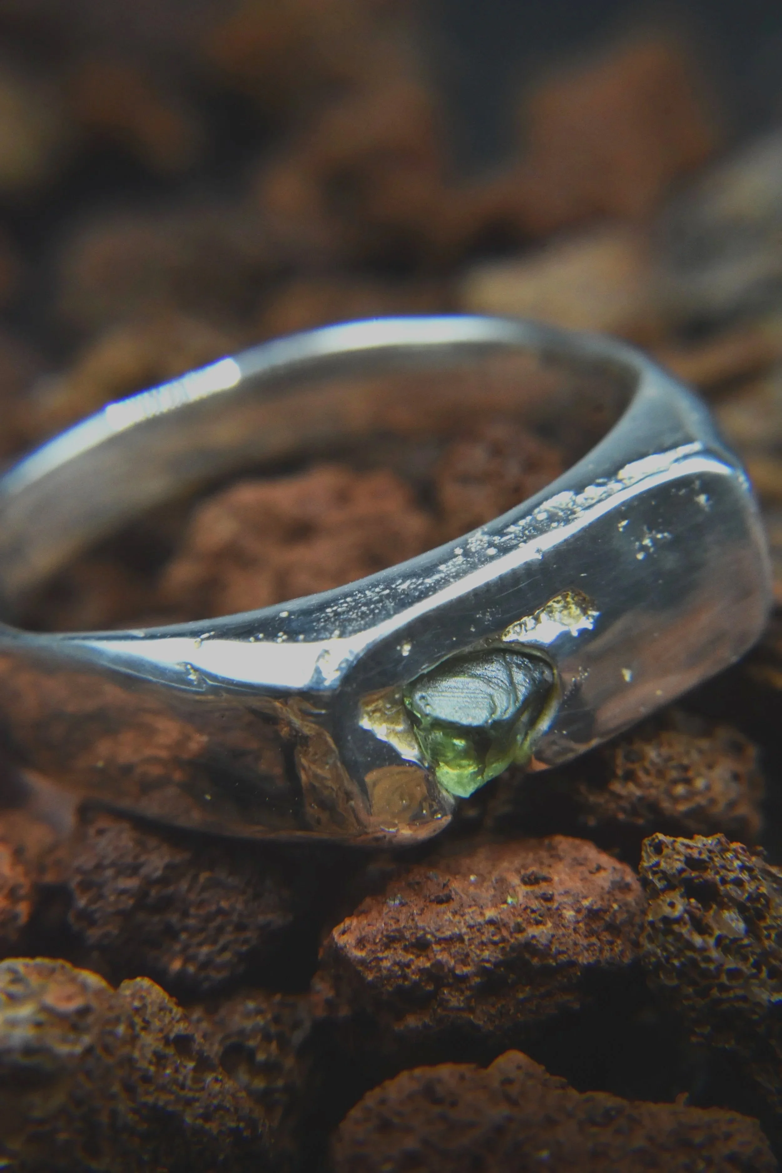 Close-up of a silver ring with a green gemstone set on a rough brown surface.