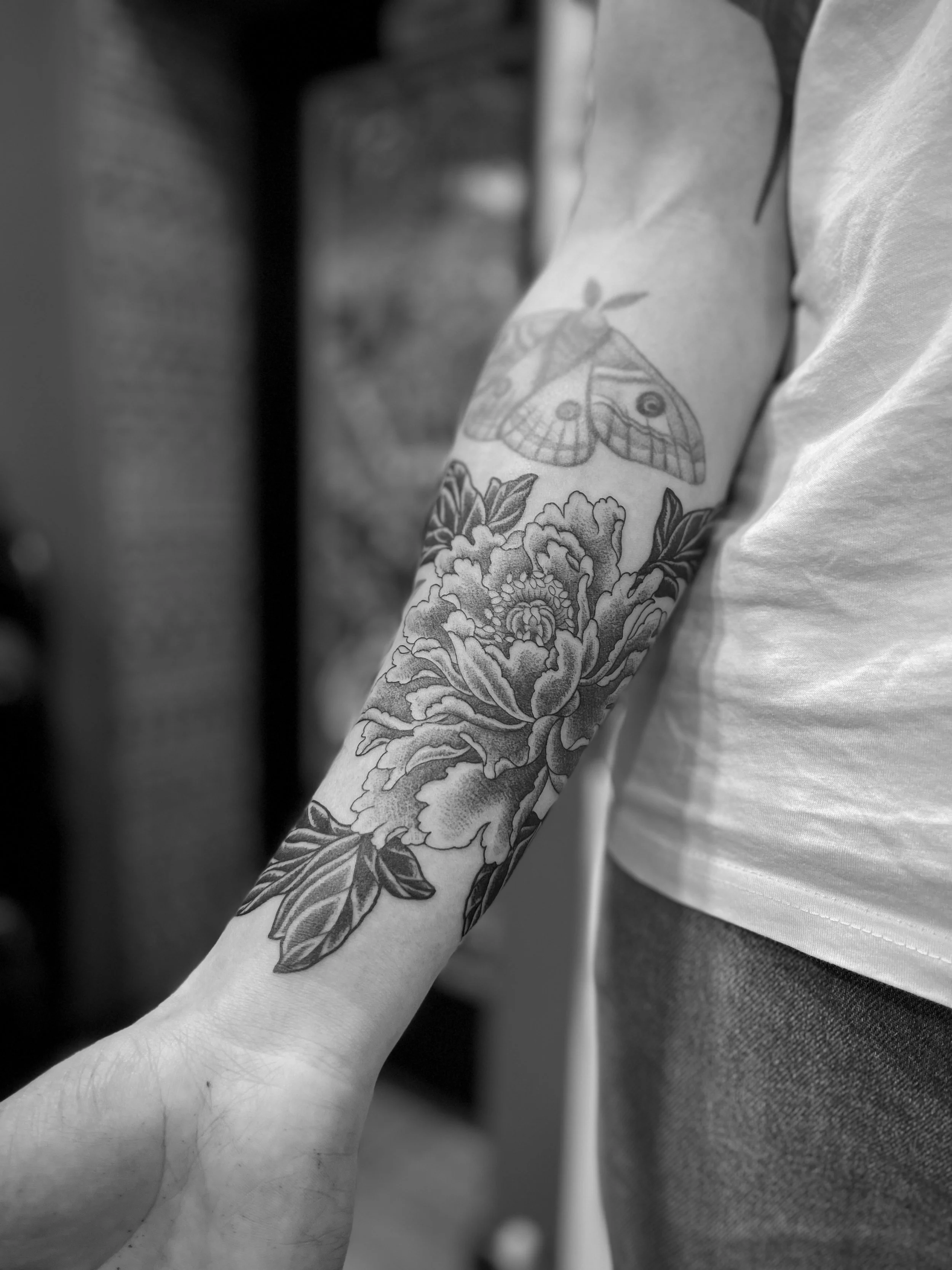 Fine line black and grey tattoo of a peony on the forearm, in Soho, central London.