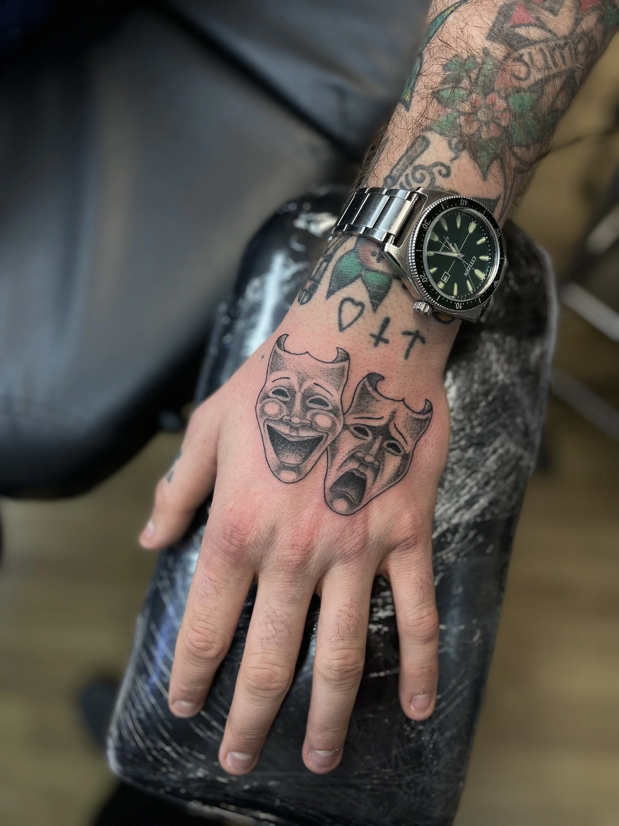 Fine line theatre masks tattoo on the hand, done at Frith Street Tattoos, Soho, central London.