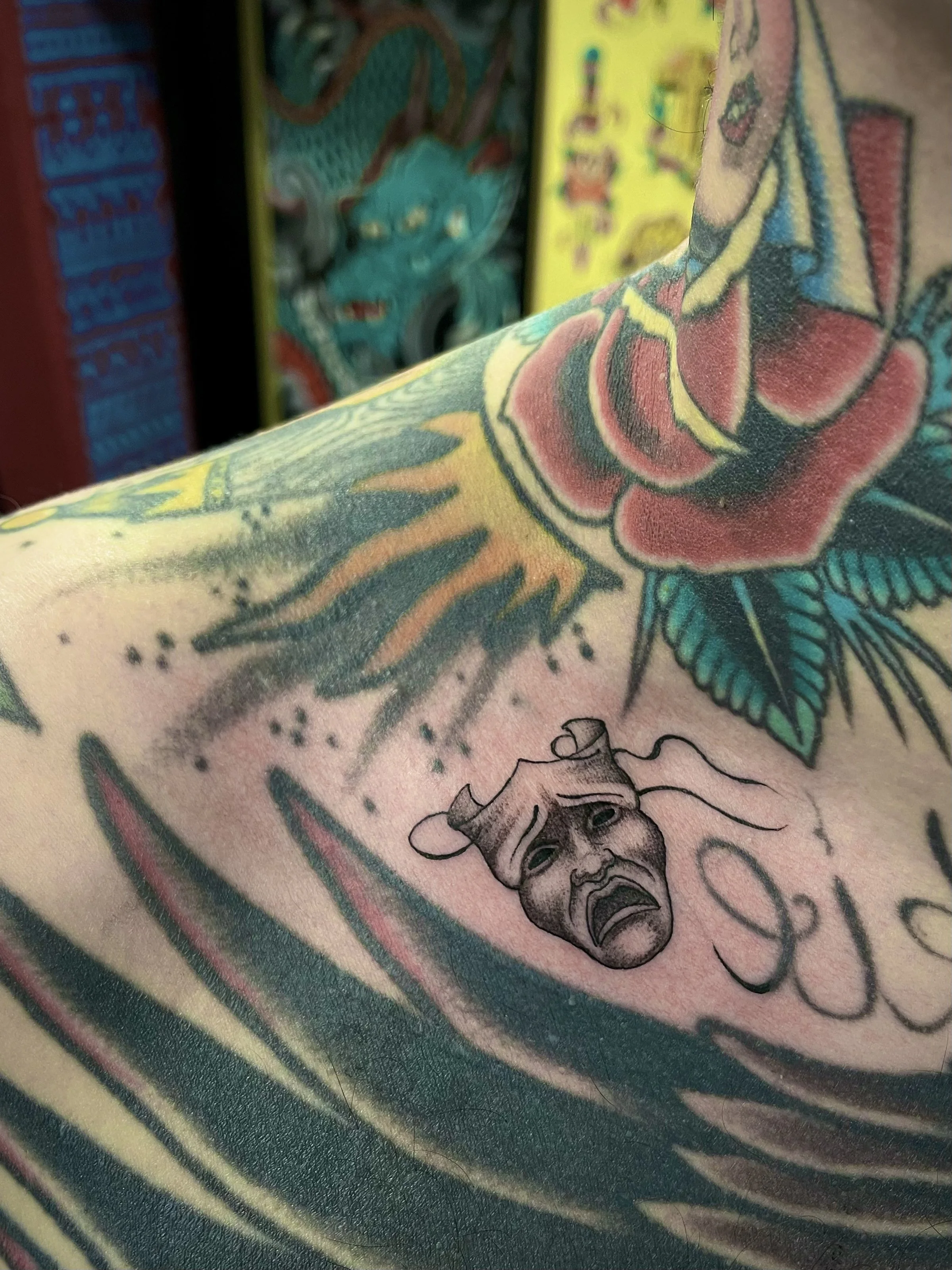 Fine line, black and grey crying theatre mask tattoo on the collar bone, done at Frith Street Tattoos, Soho, central London.