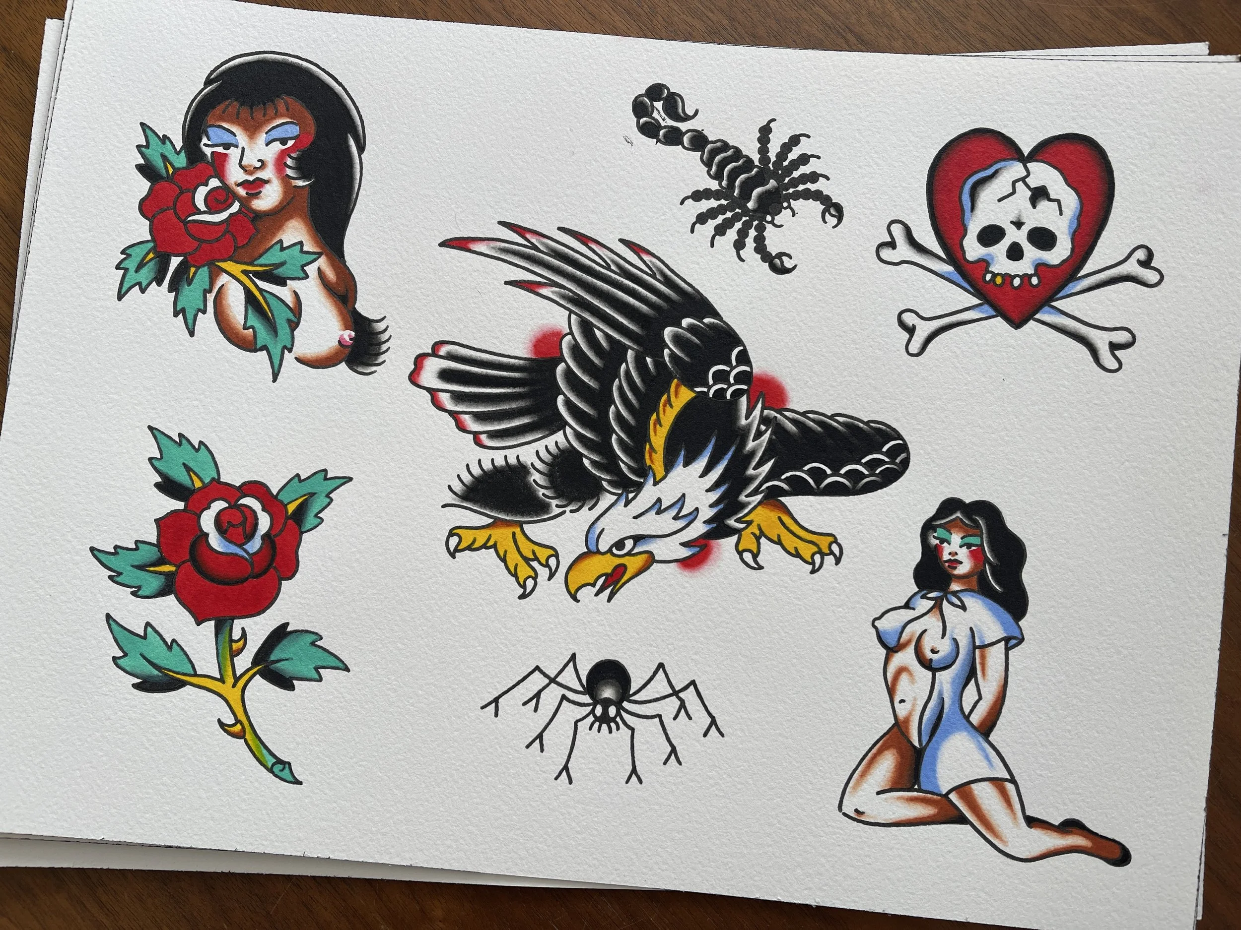 Traditional tattoo flash sheet of eagle, scorpion, spider, girls, skull, heart and rose, designs available to be tattooed at Frith Street Tattoos, Soho, London