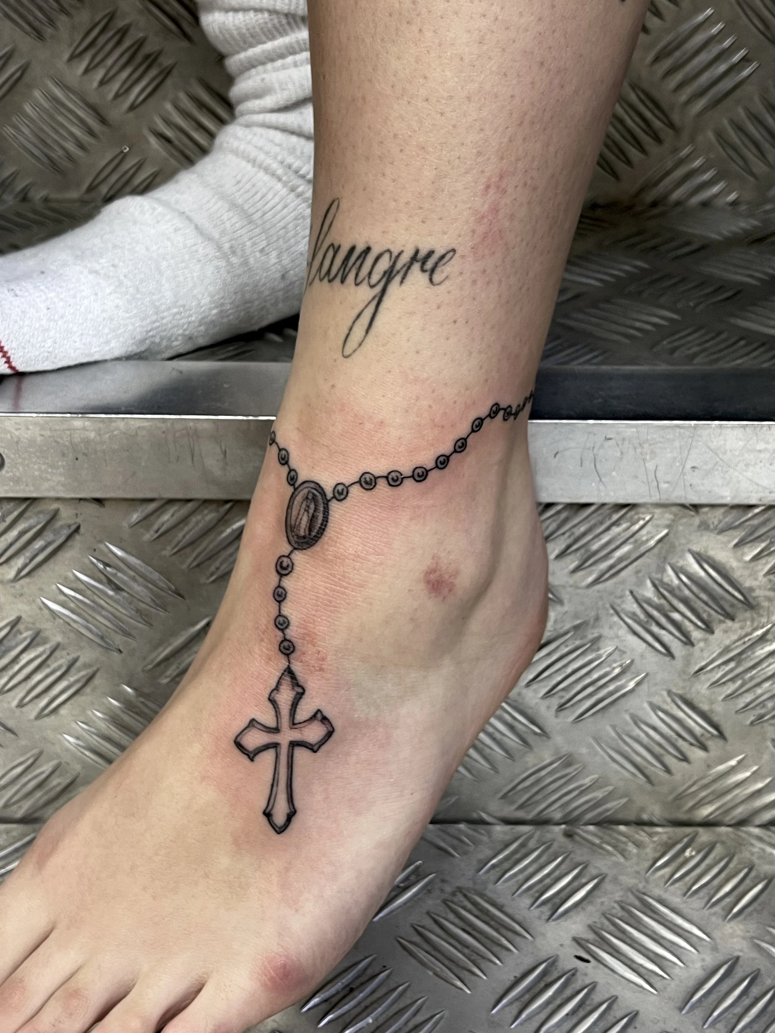 Fine line black and grey rosary bead tattoo round the ankle, done at Frith Street Tattoos, Soho, central London.