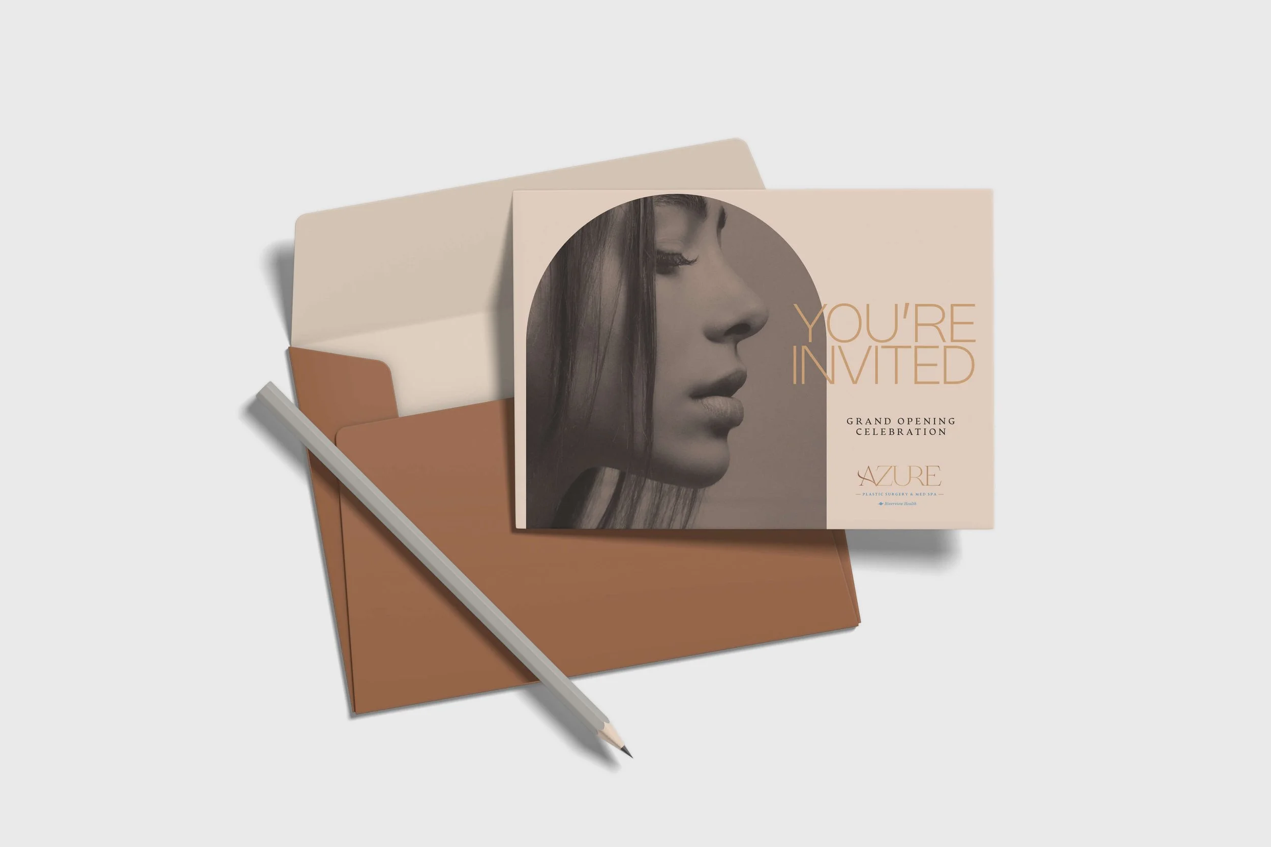 Invitation card with a woman's profile photo, the text 'You're Invited' and details for a grand opening celebration from Azure Plastic Surgery & Med Spa, placed on a brown envelope with a pen nearby.