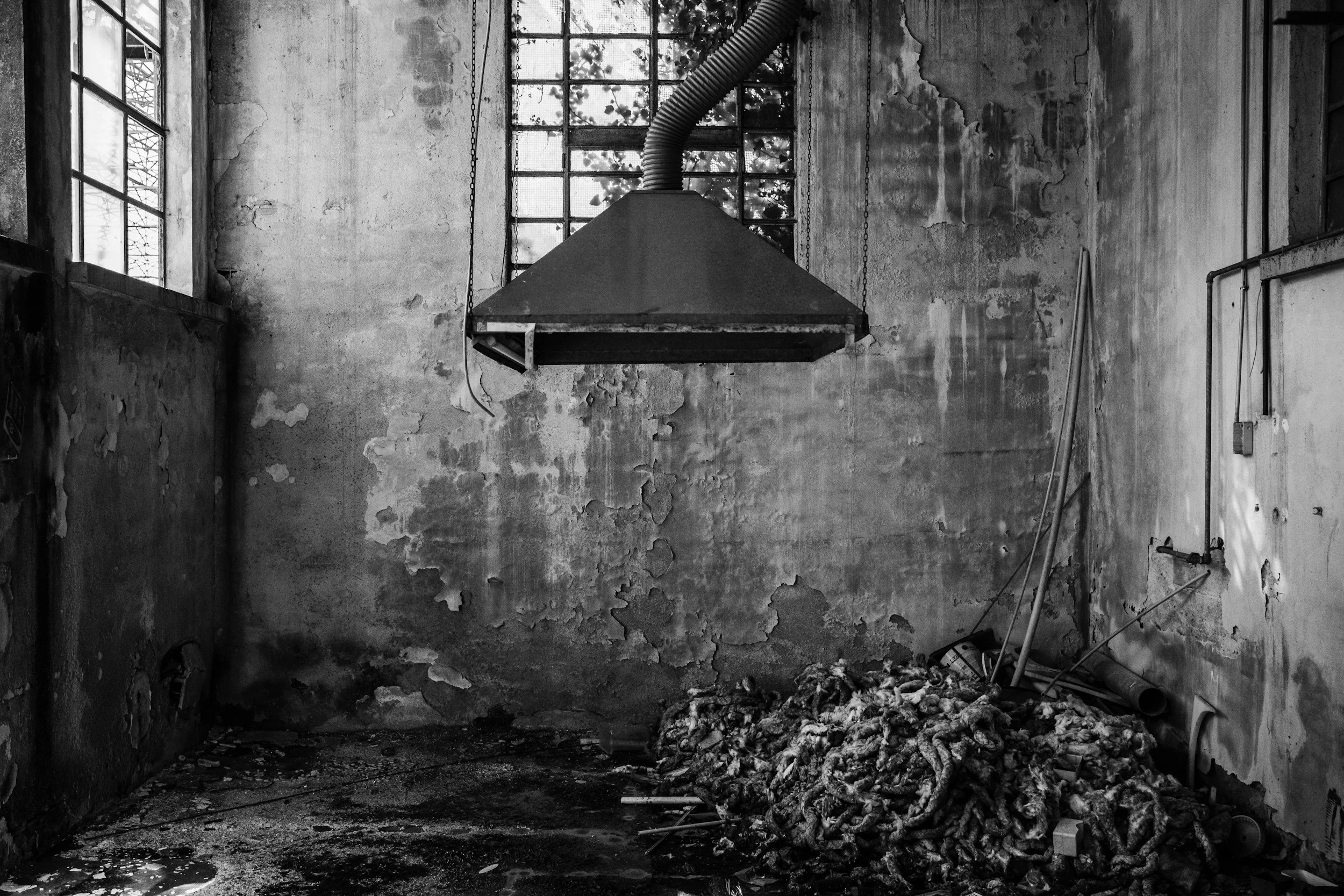 An abandoned, dilapidated room with peeling walls, broken windows, and debris on the floor, including a pile of insulation and scattered wires.