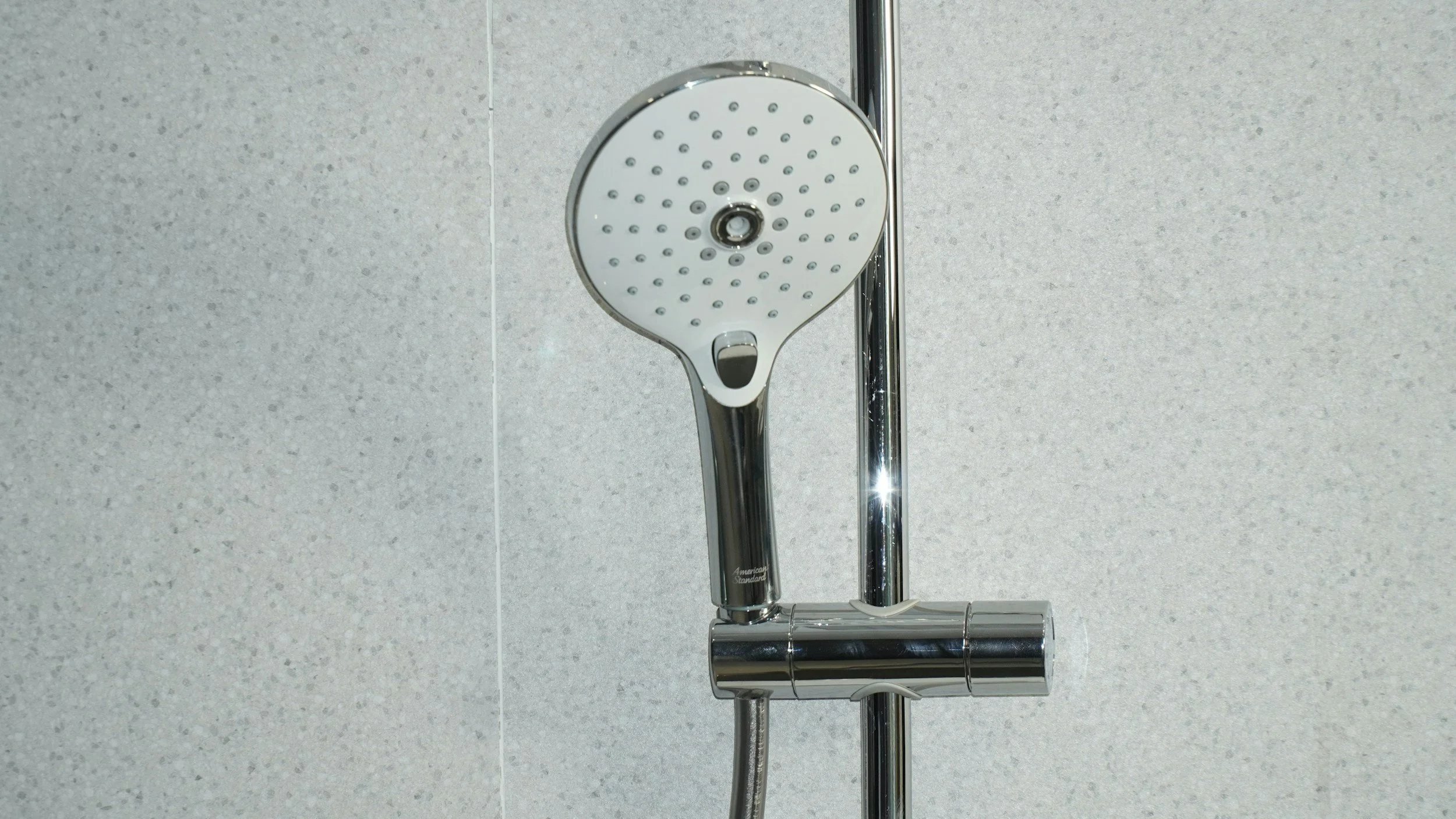 Shower head mounted on a tiled bathroom wall with a chrome pipe extending below.