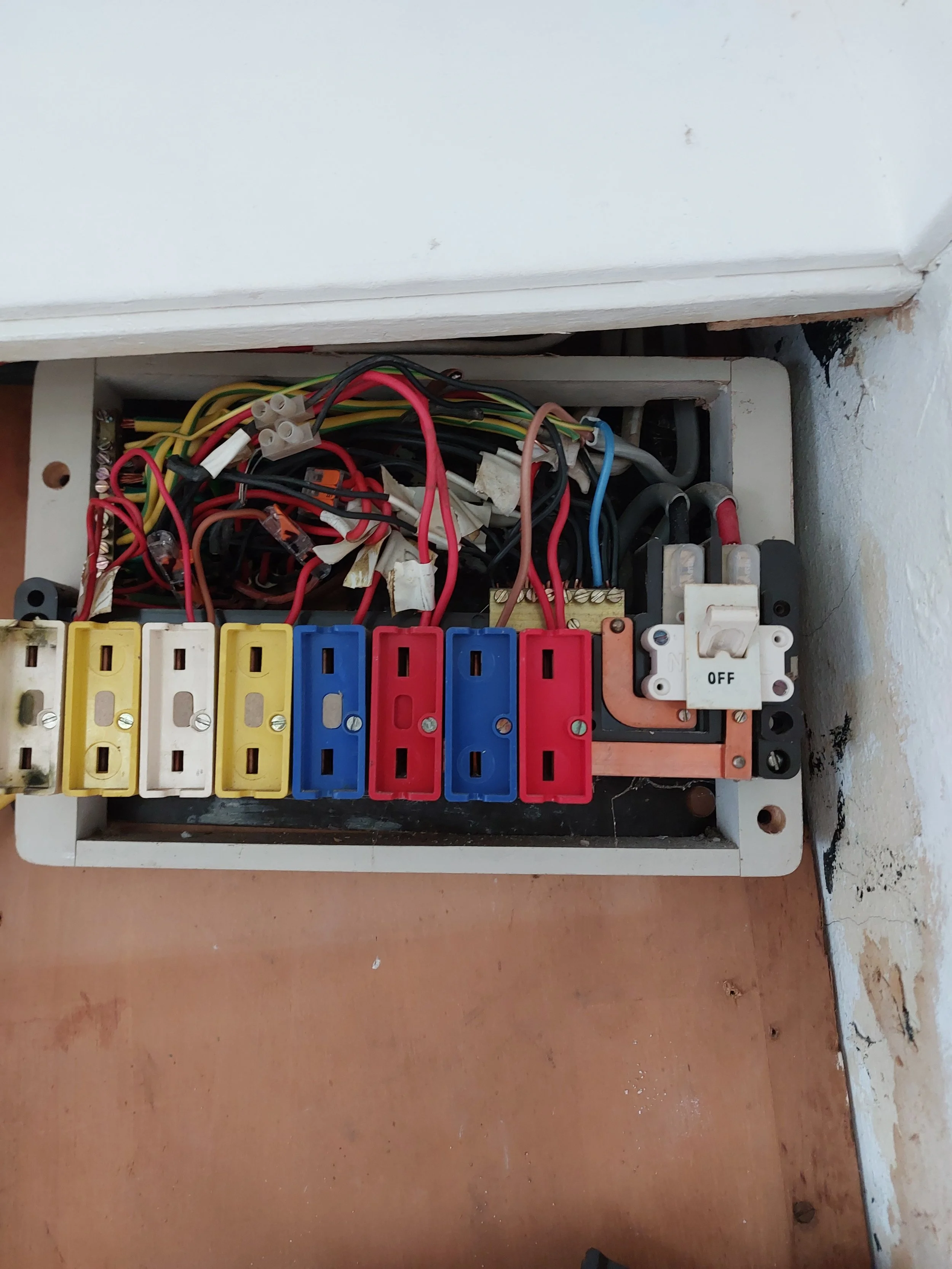 An electrical breaker box with colored wires and switches inside, mounted on a wall.