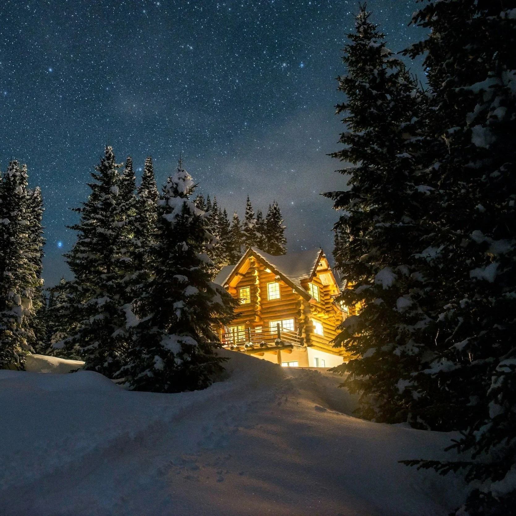 A cozy illuminated log cabin in a snowy forest at night with a clear starry sky overhead.