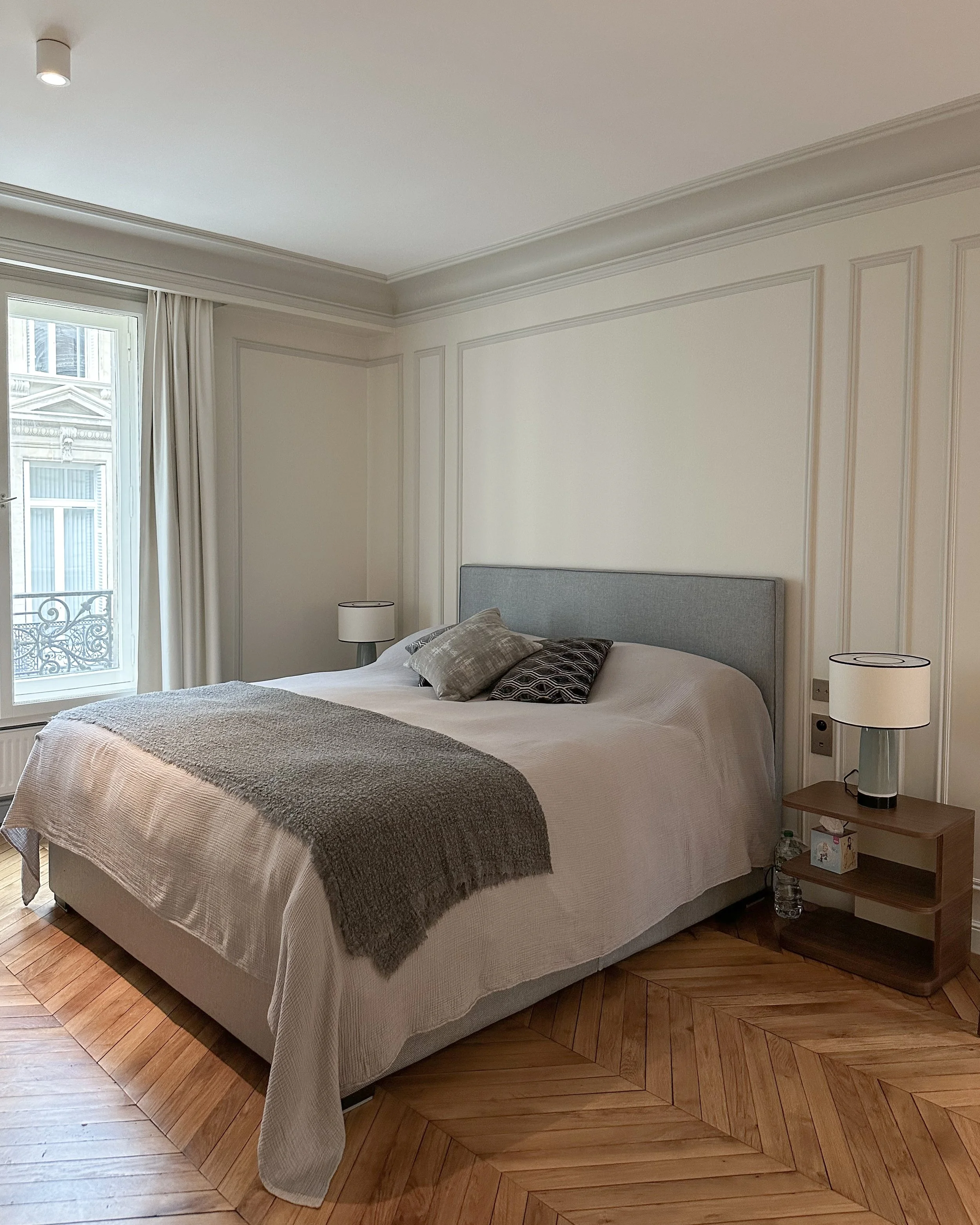Chambre avec lit, deux lampes de nuit, fenêtres, parquet en bois.