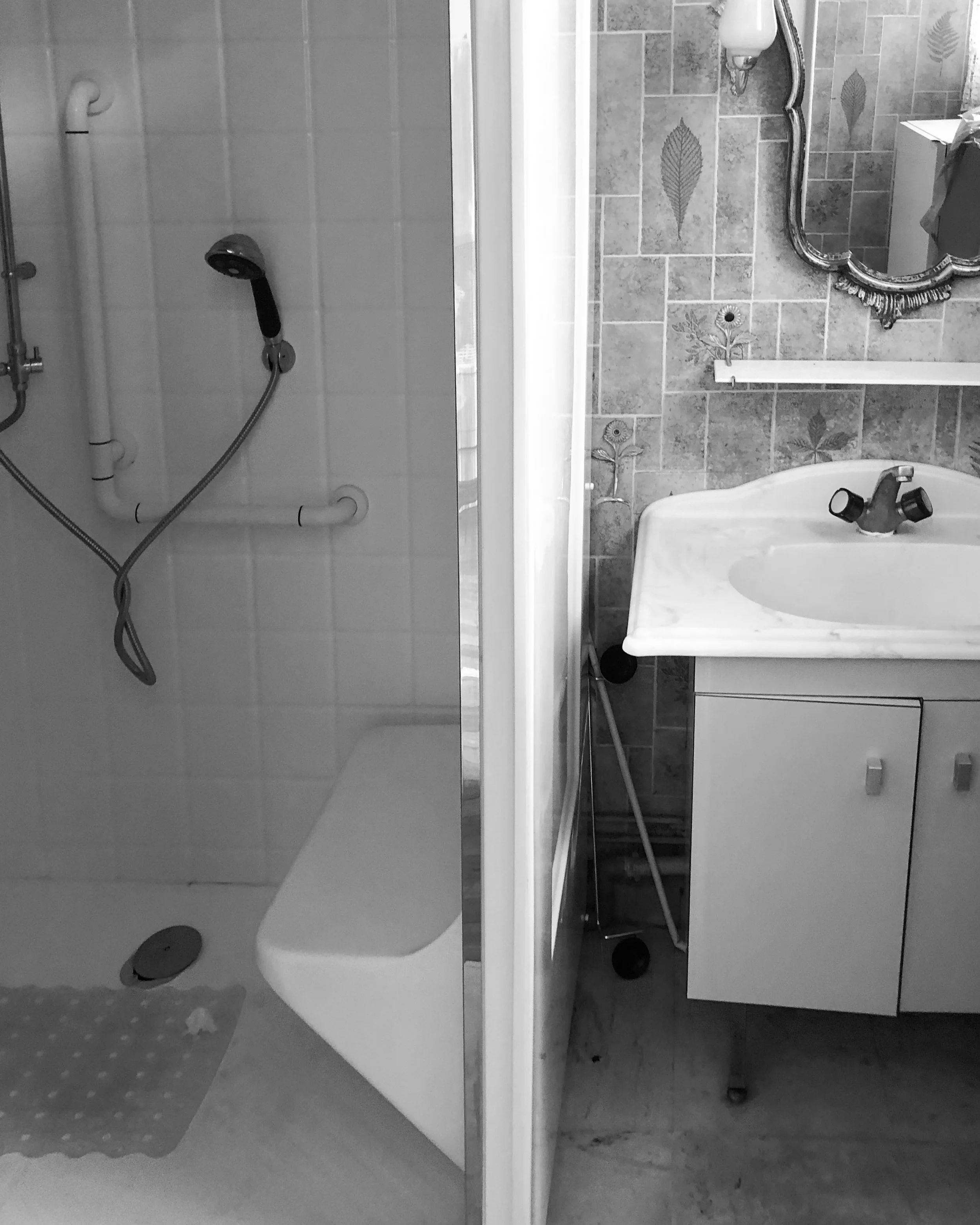 Une salle de bain séparée en deux parties, une avec une douche (partie gauche) et l'autre avec un lavabo et un miroir (partie droite).