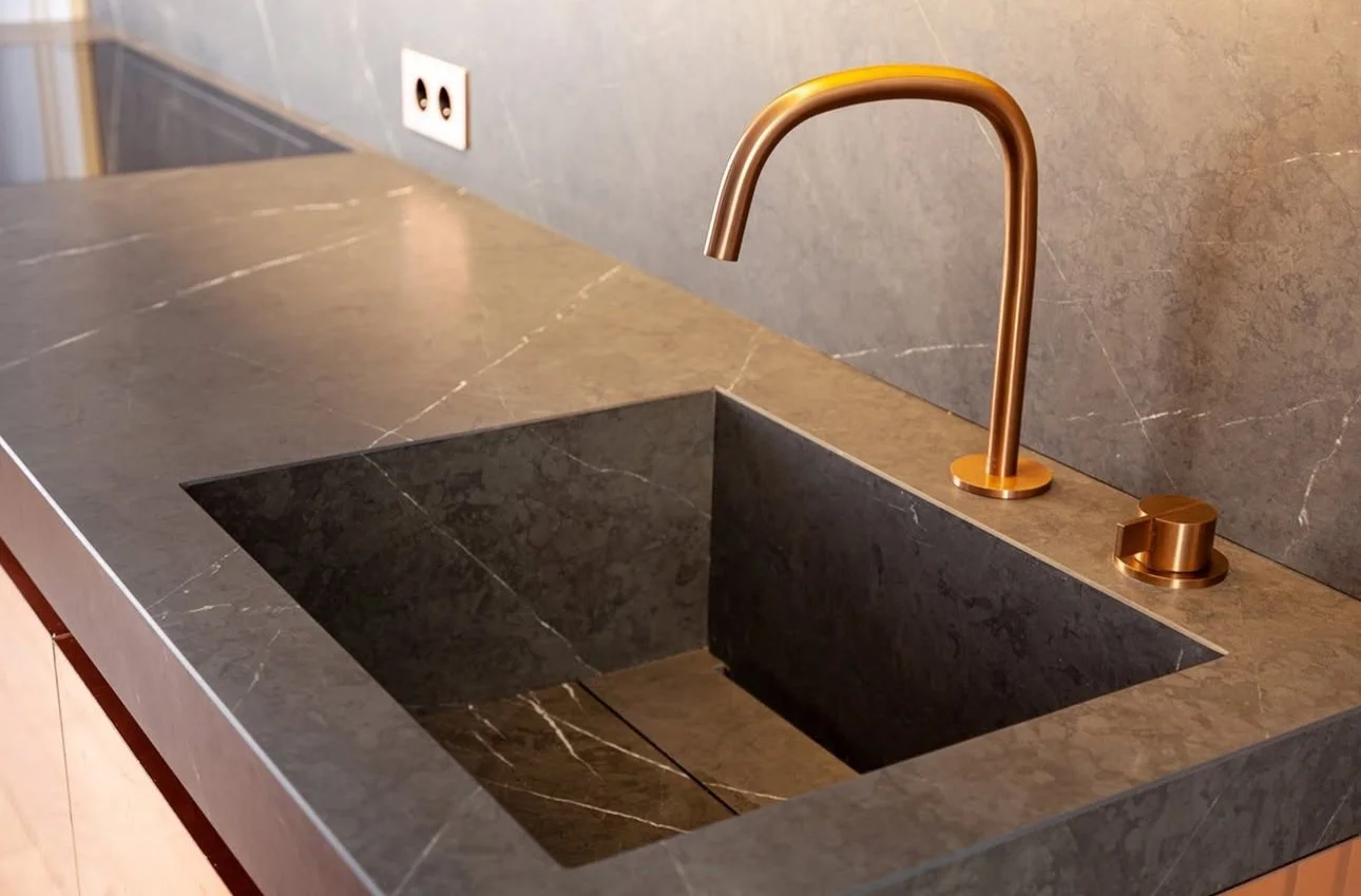 Évier noir en marbre avec robinet en métal bronze, dans une cuisine moderne.