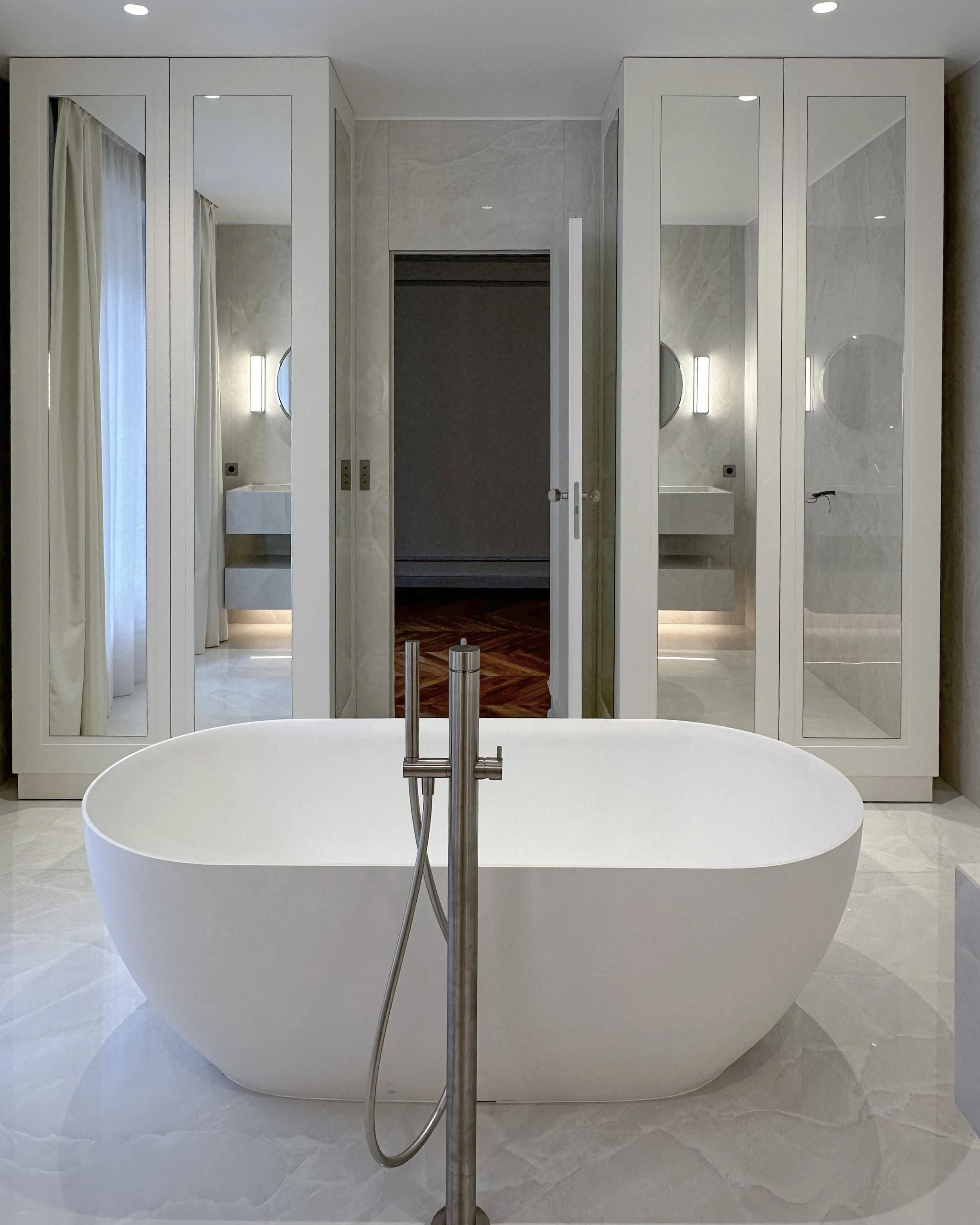 Bain en îlot blanc dans une salle de bain élégante avec armoires en miroir et murs en pierre claire.