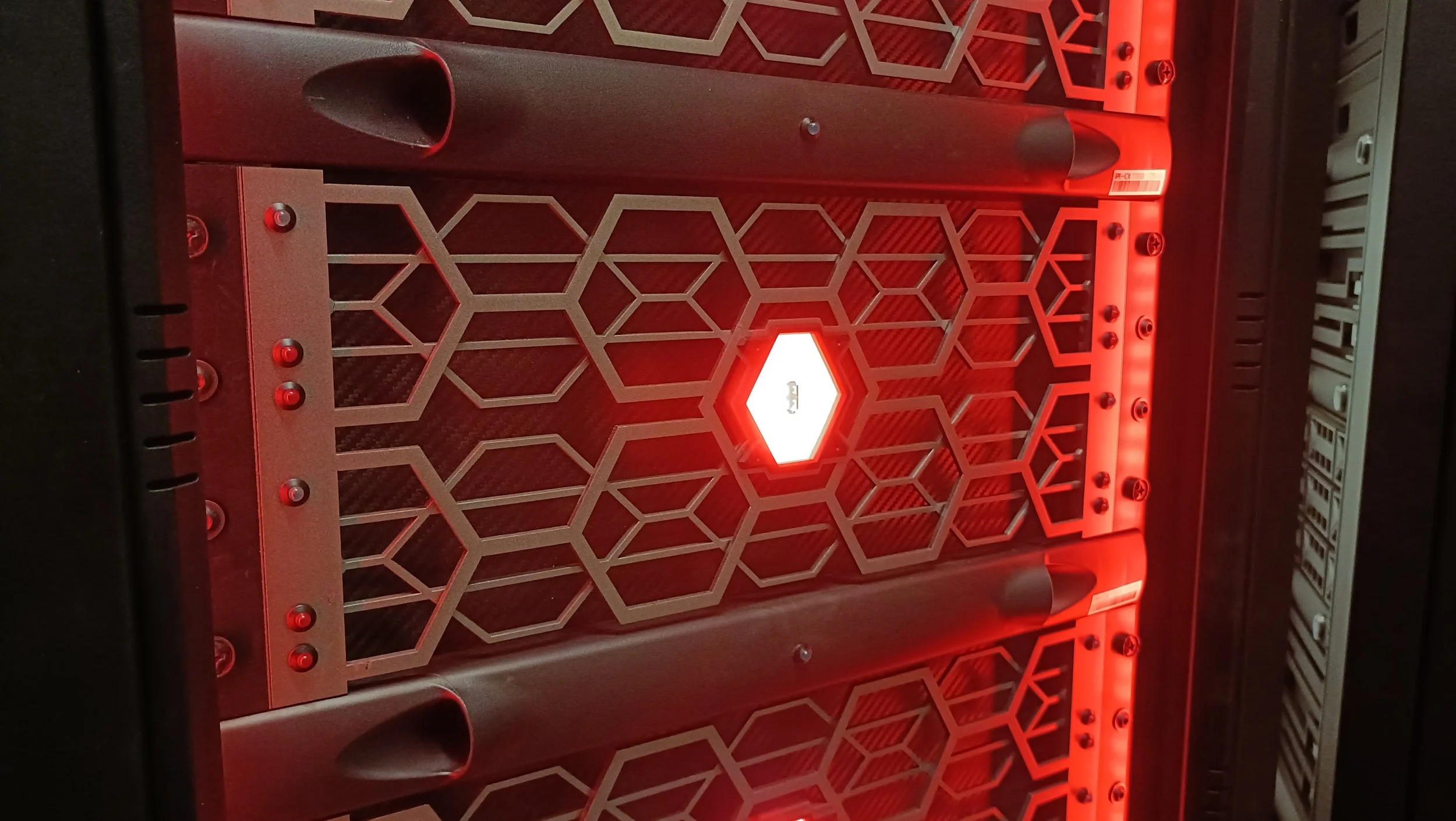 Inside a computer server case with a metal honeycomb vent and red LED lighting.
