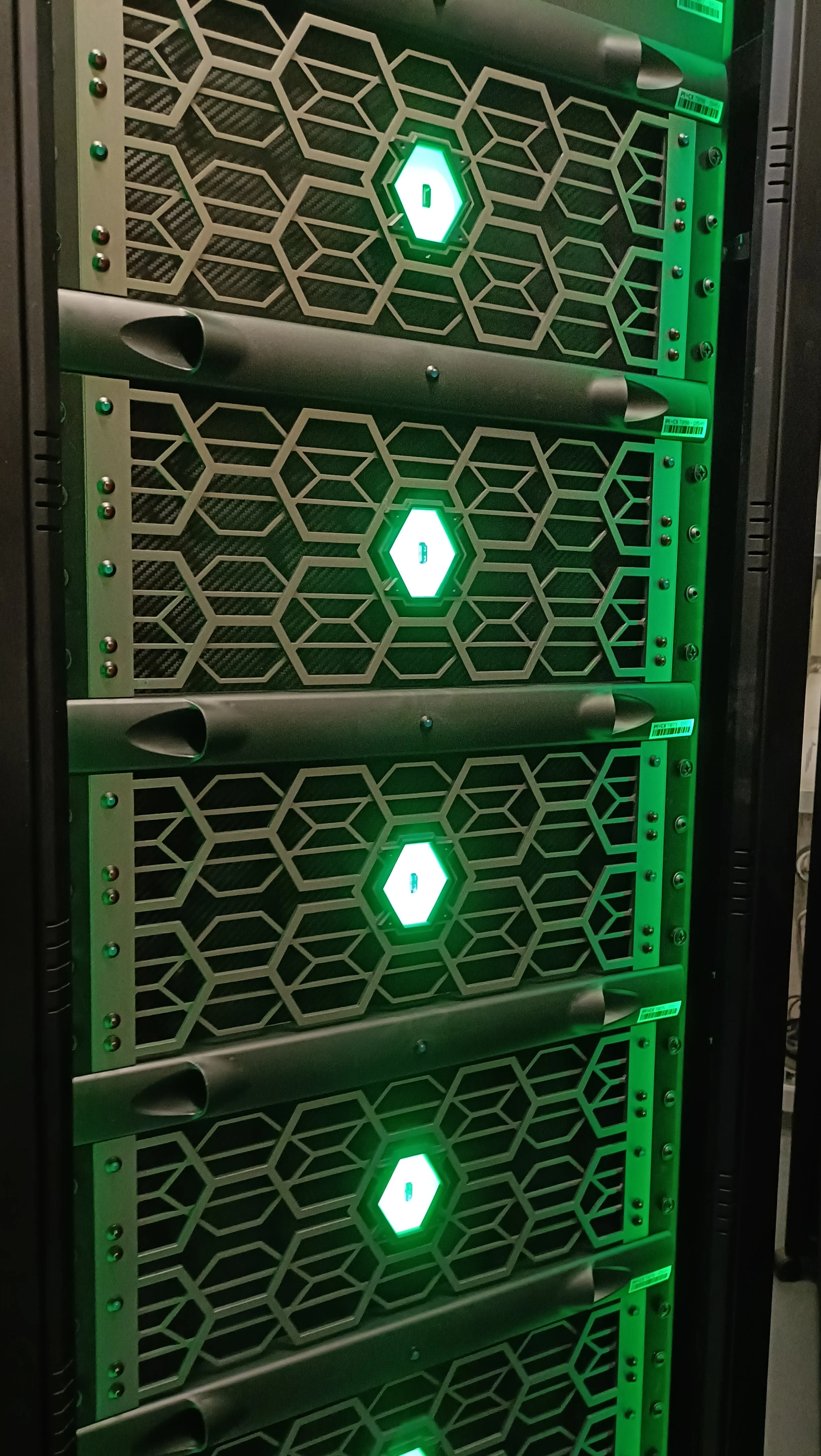 A server rack with multiple server units, each featuring a green LED light and a geometric pattern on the front panel.