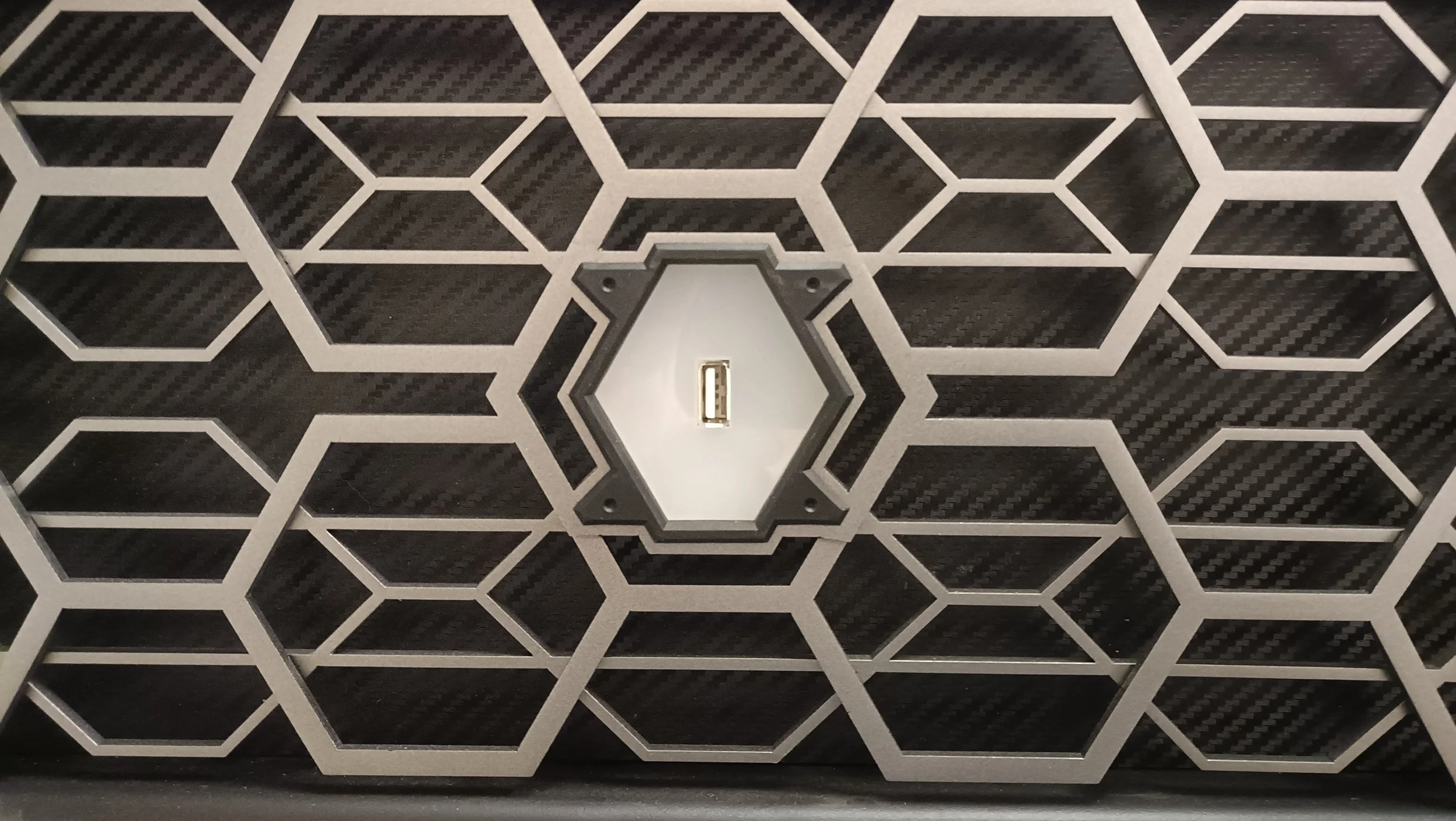 Close-up of a hexagonal patterned surface with a central USB port in a black and silver color scheme.