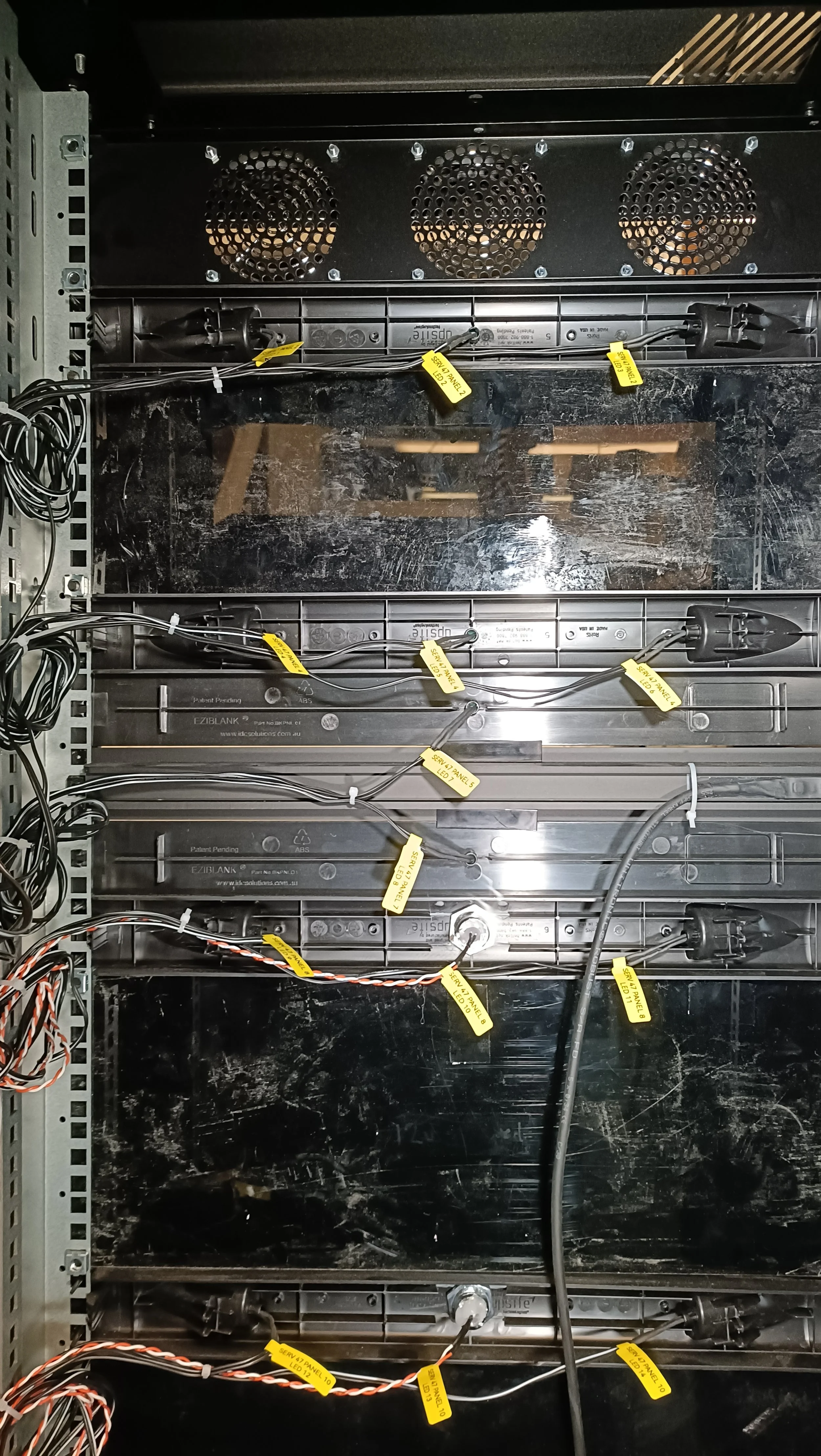 Open electronic panel with wiring and yellow tags on cables.