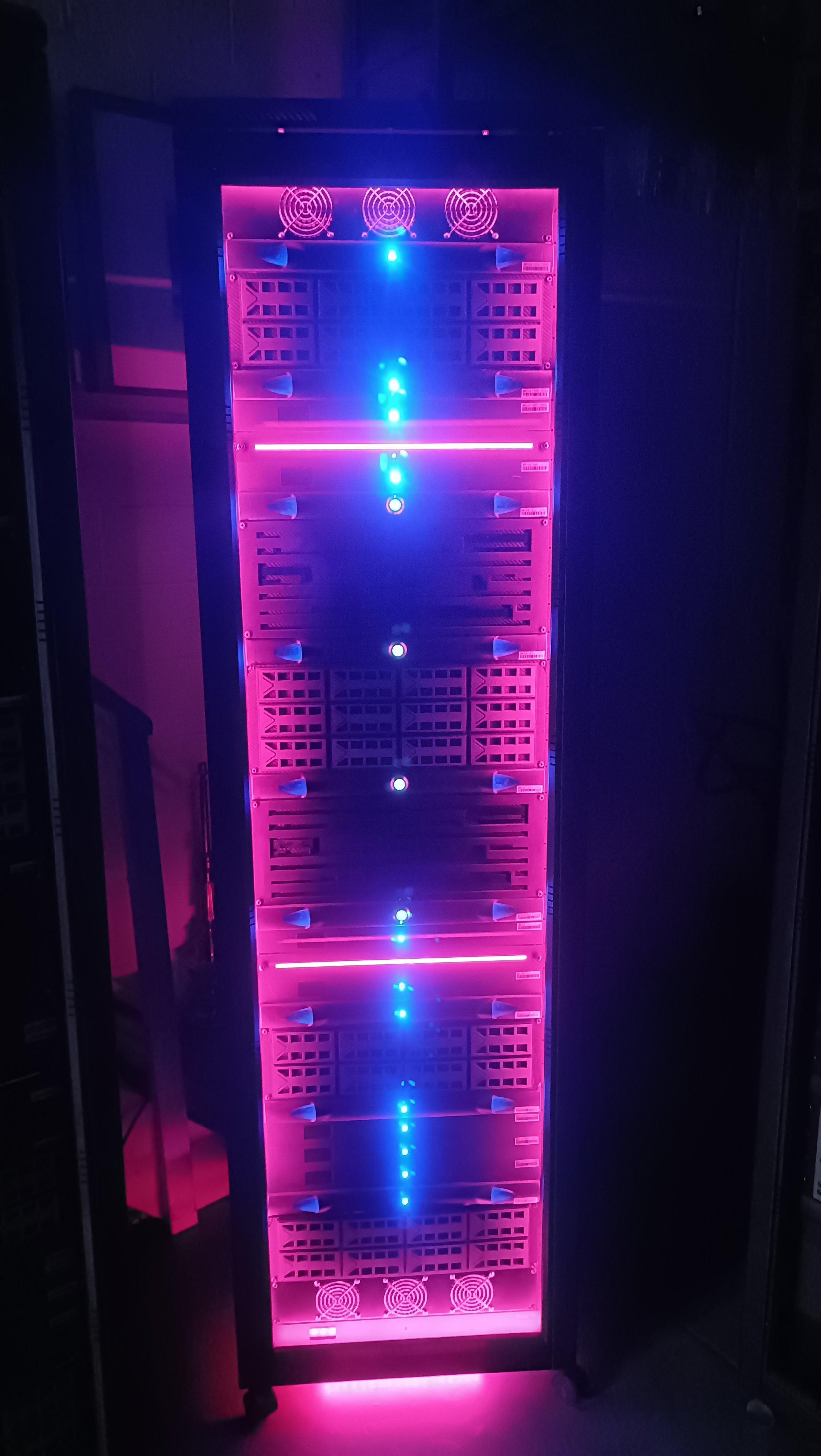 A server rack with pink and blue LED lights and cooling fans.