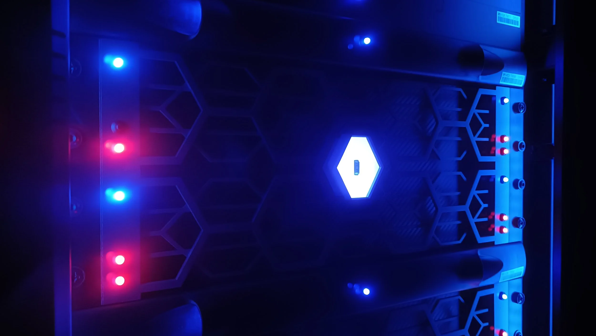 Close-up of a gaming console with blue and red LED lights, featuring a hexagonal design pattern and a central glowing hexagon.