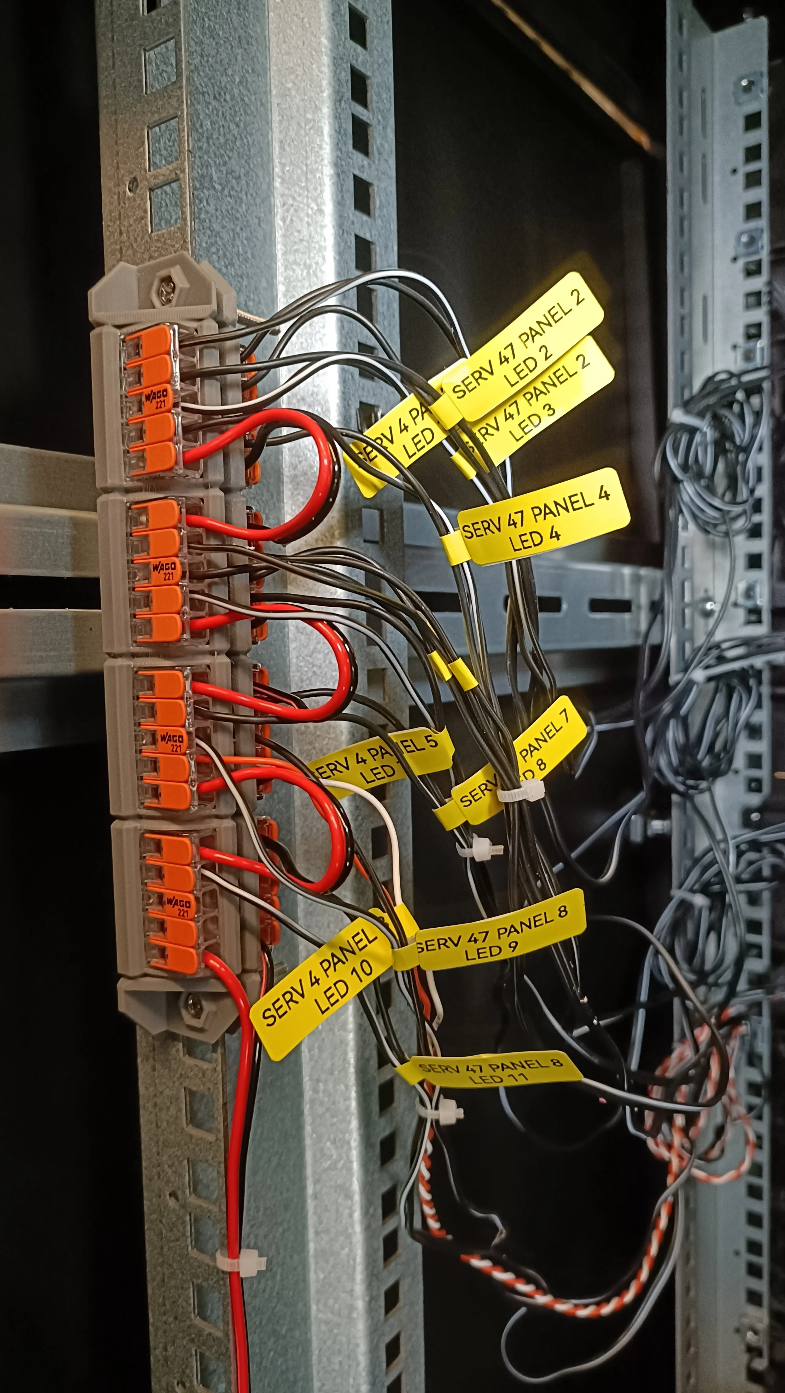 Close-up view of a server rack with multiple wires connected to a terminal block and yellow labels indicating connections for different panels and LED indicators.