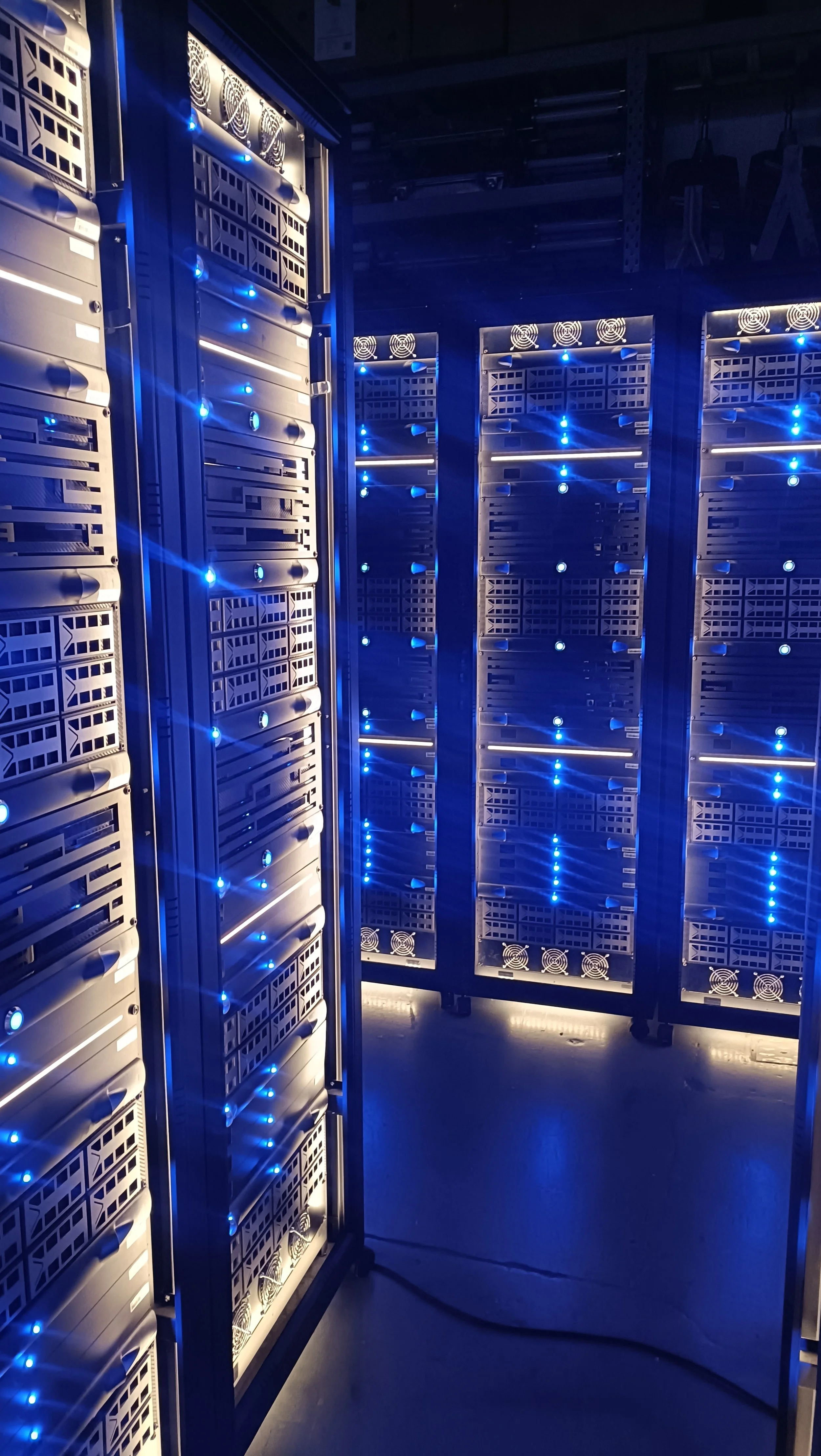 A row of black server racks with blue LED lights inside a data center.