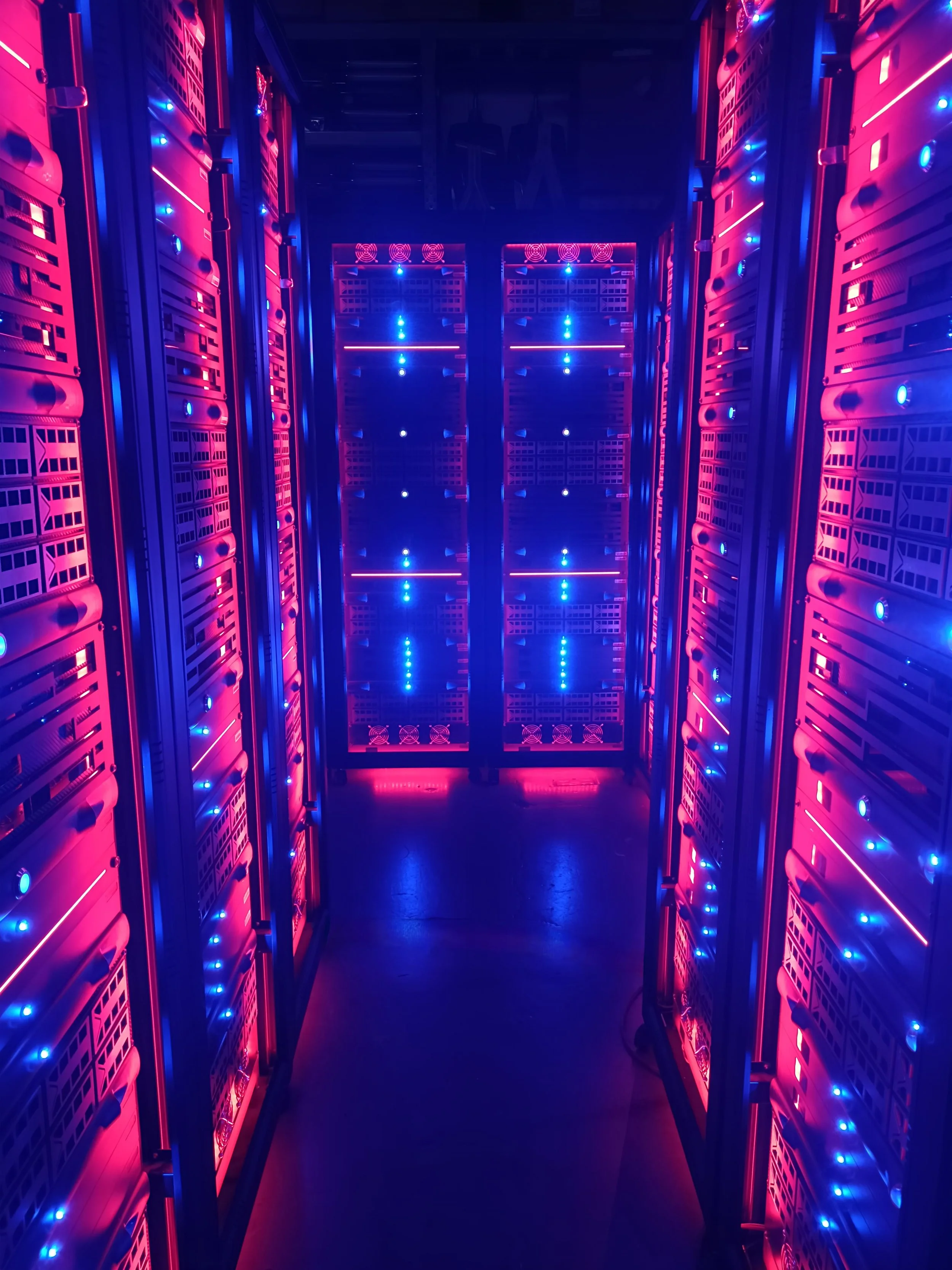 A hallway filled with server racks illuminated by pink and blue LED lights, creating a futuristic, technology-rich environment.