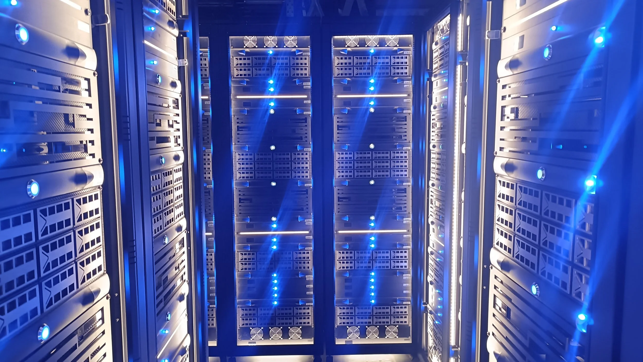 Inside a data center or server room with multiple racks of computer servers illuminated by blue LED lights, with visible cooling fans.