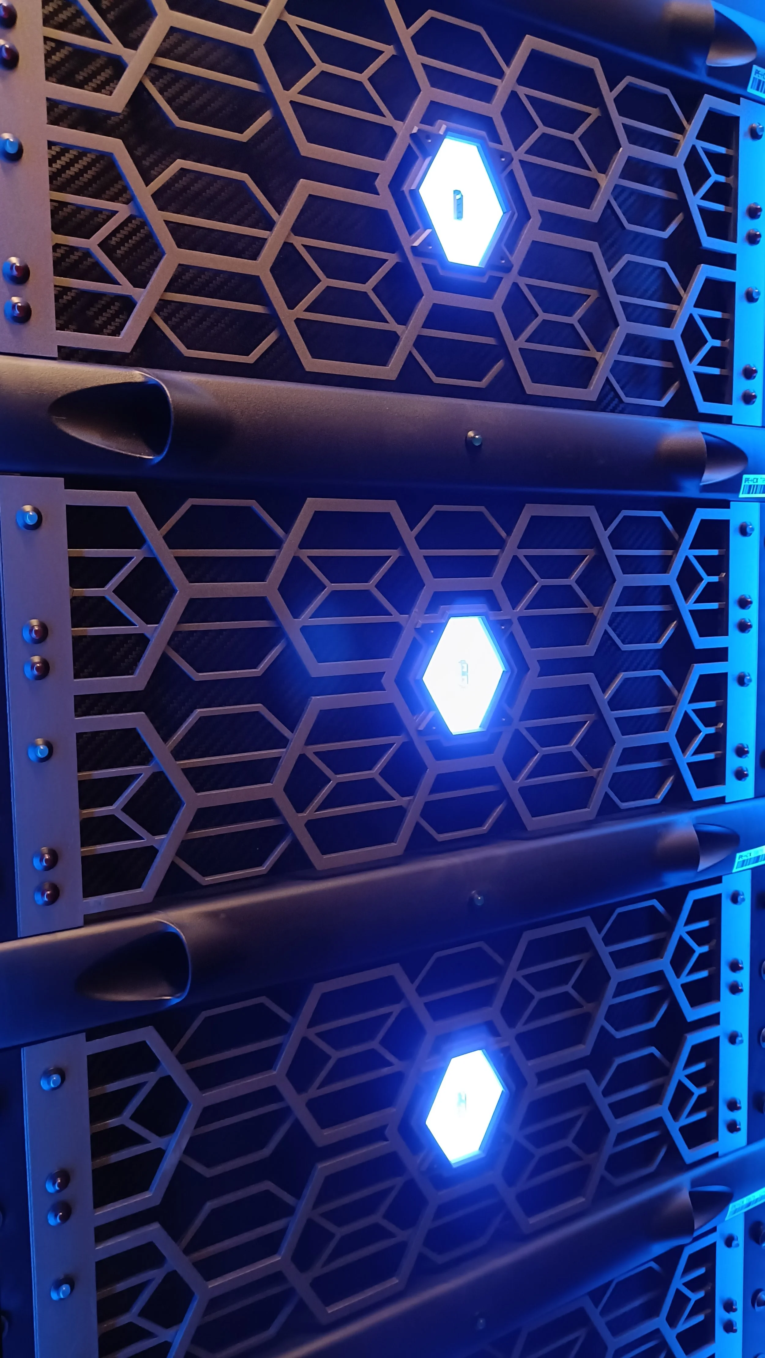 Close-up view of three server hardware units with black metal grates, each with a bright blue LED light and honeycomb design, mounted on a rack in a data center.