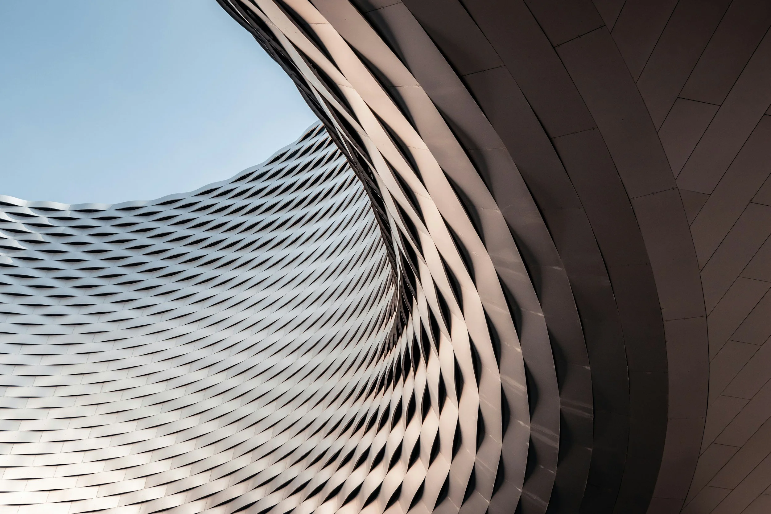 Vue en contre-plongée d'une façade architecturale moderne avec des motifs ondulés en métal et un ciel clair en fond.