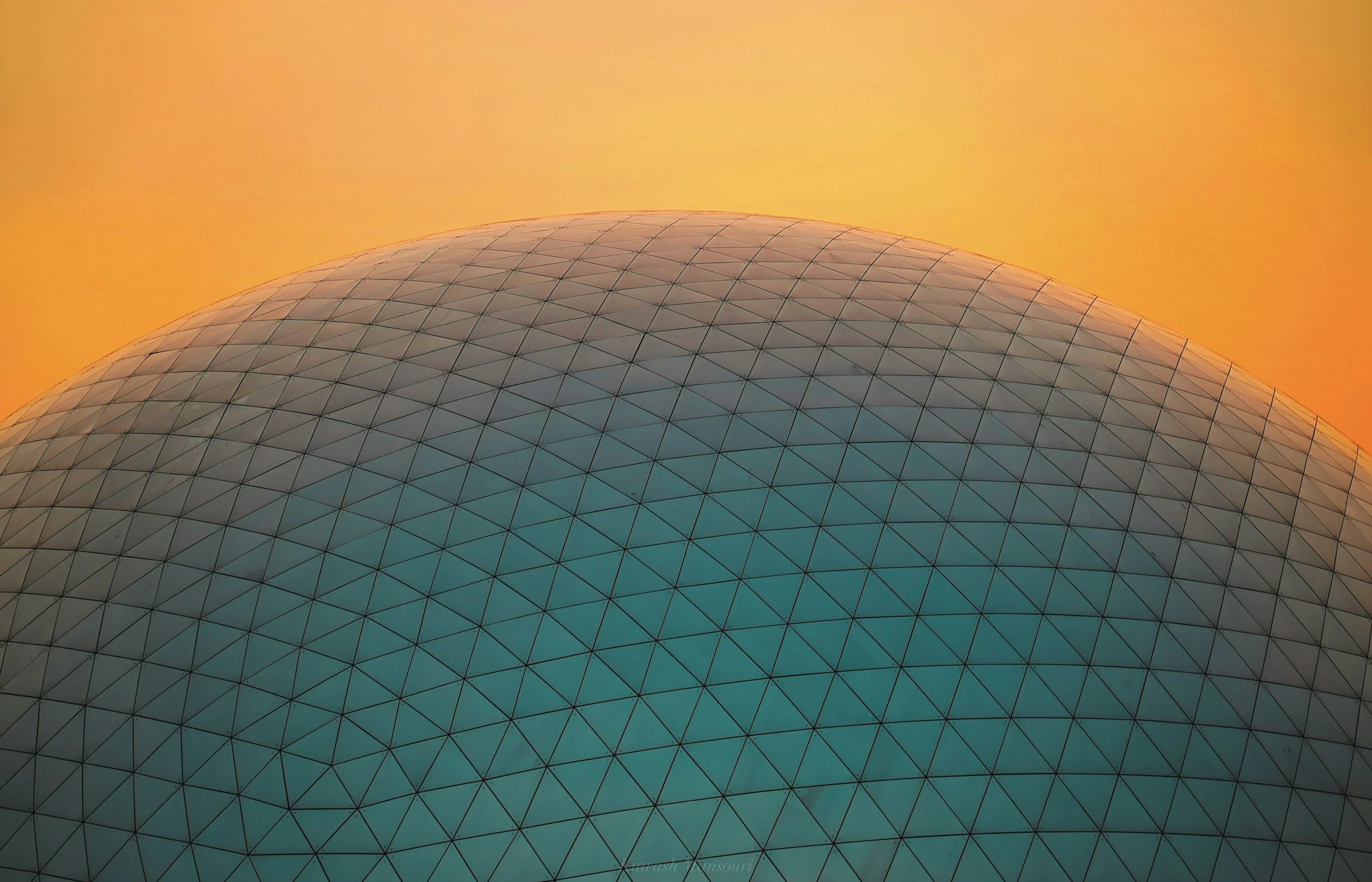 Une structure géodésique en forme de dôme avec un ciel orange en arrière-plan.
