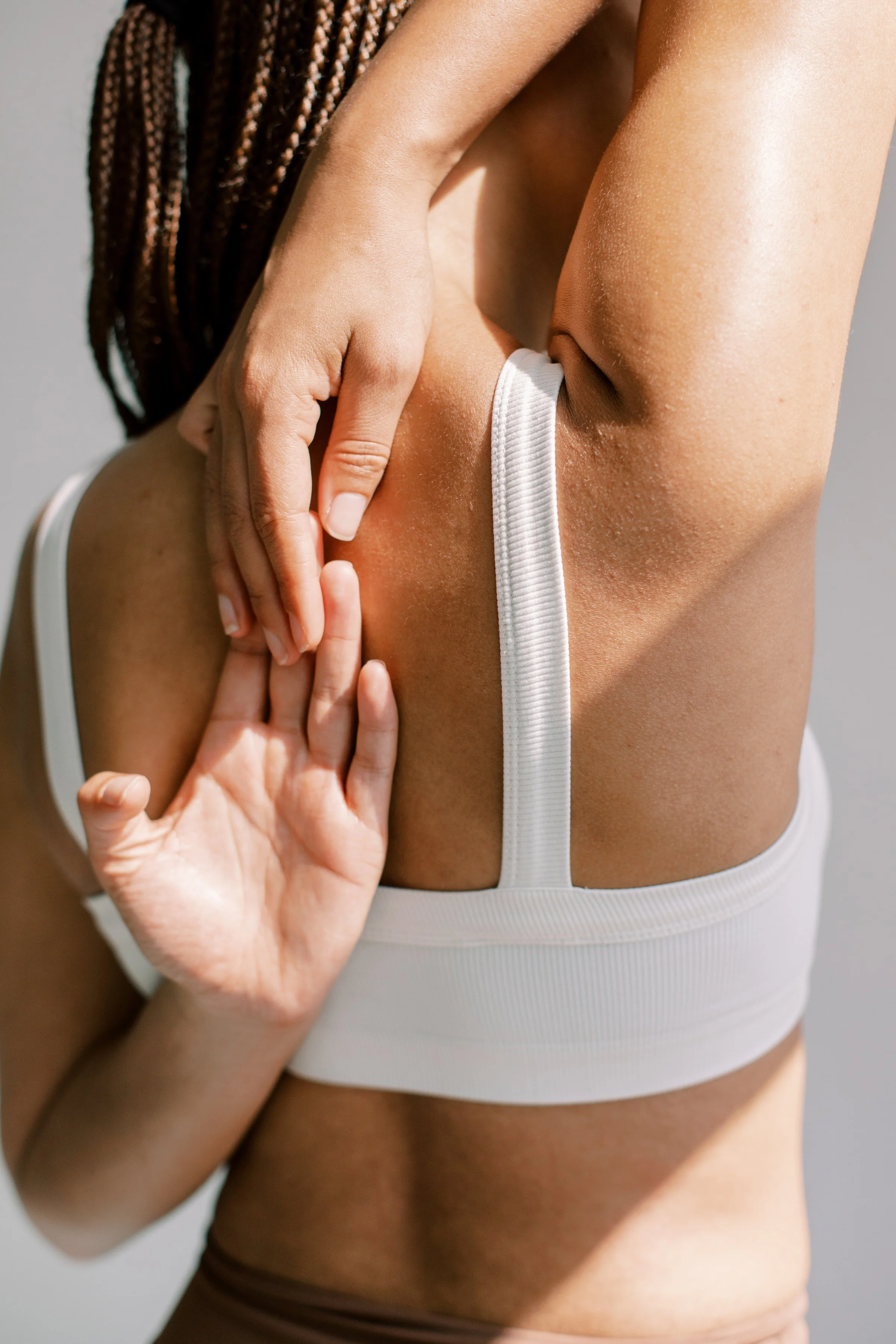 A person scratching their armpit with their hand, wearing a white sports bra.