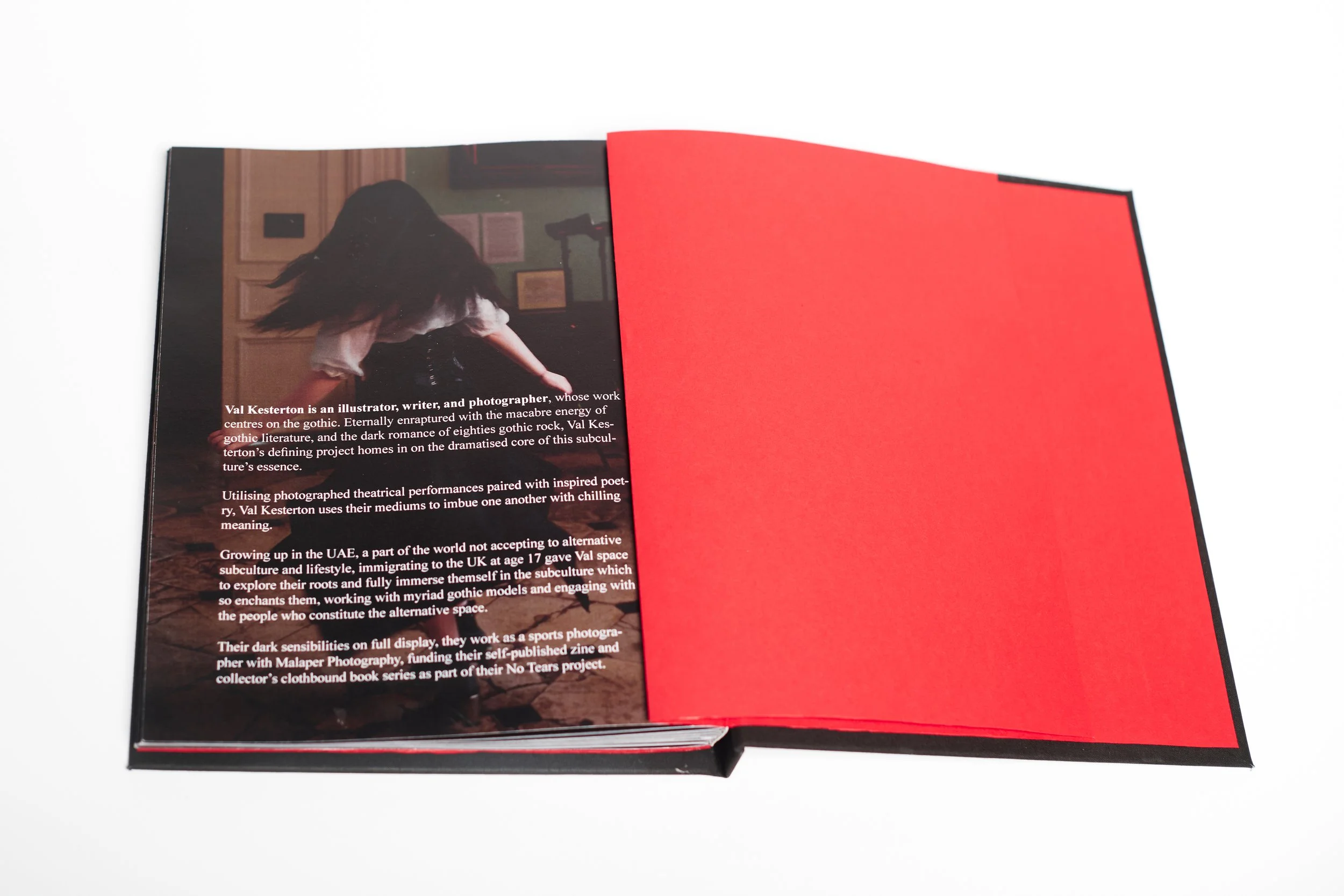 Open magazine with text and a photograph of a person with long hair, sitting on a wooden floor against a green wall with framed pictures. The right page is bright red, and the left page contains a paragraph of text about Val Kesterton.