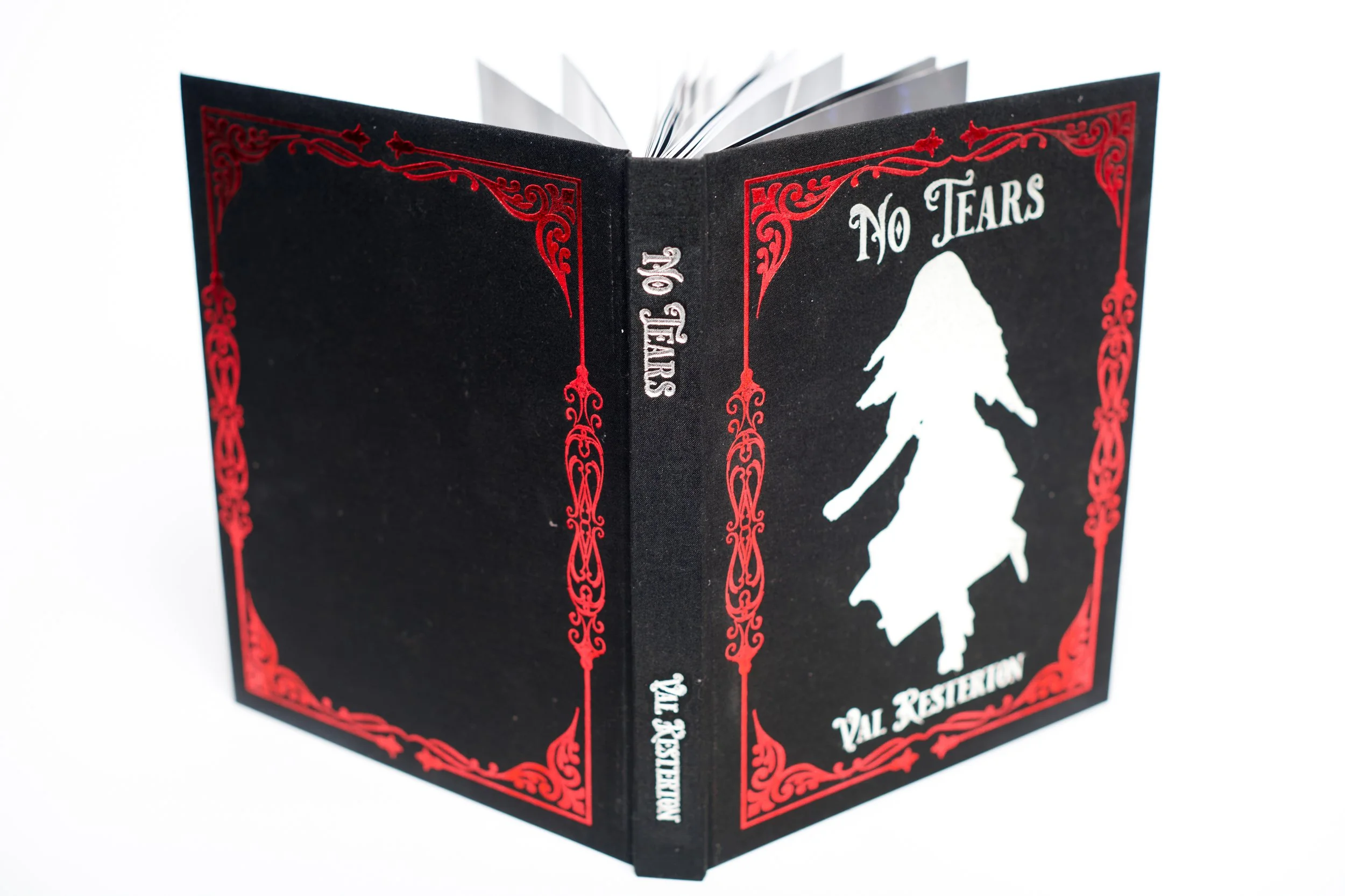 Closed black booklet titled 'No Tears' with red decorative borders and a silver silhouette of a girl in a dress on the cover.