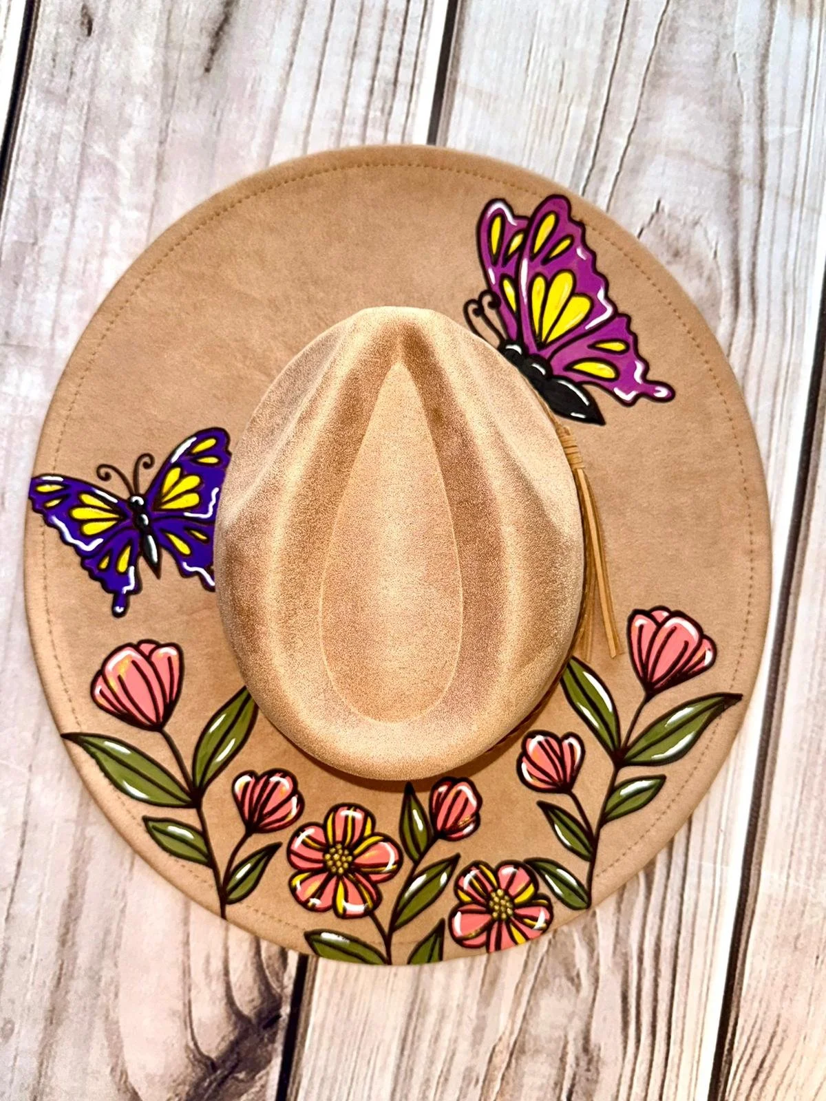 A beige cowboy hat with colorful butterfly and floral stickers, resting on a wooden surface.