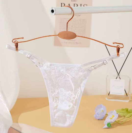White lace lingerie hanging on a copper hanger on a clothing rod in a softly lit room.