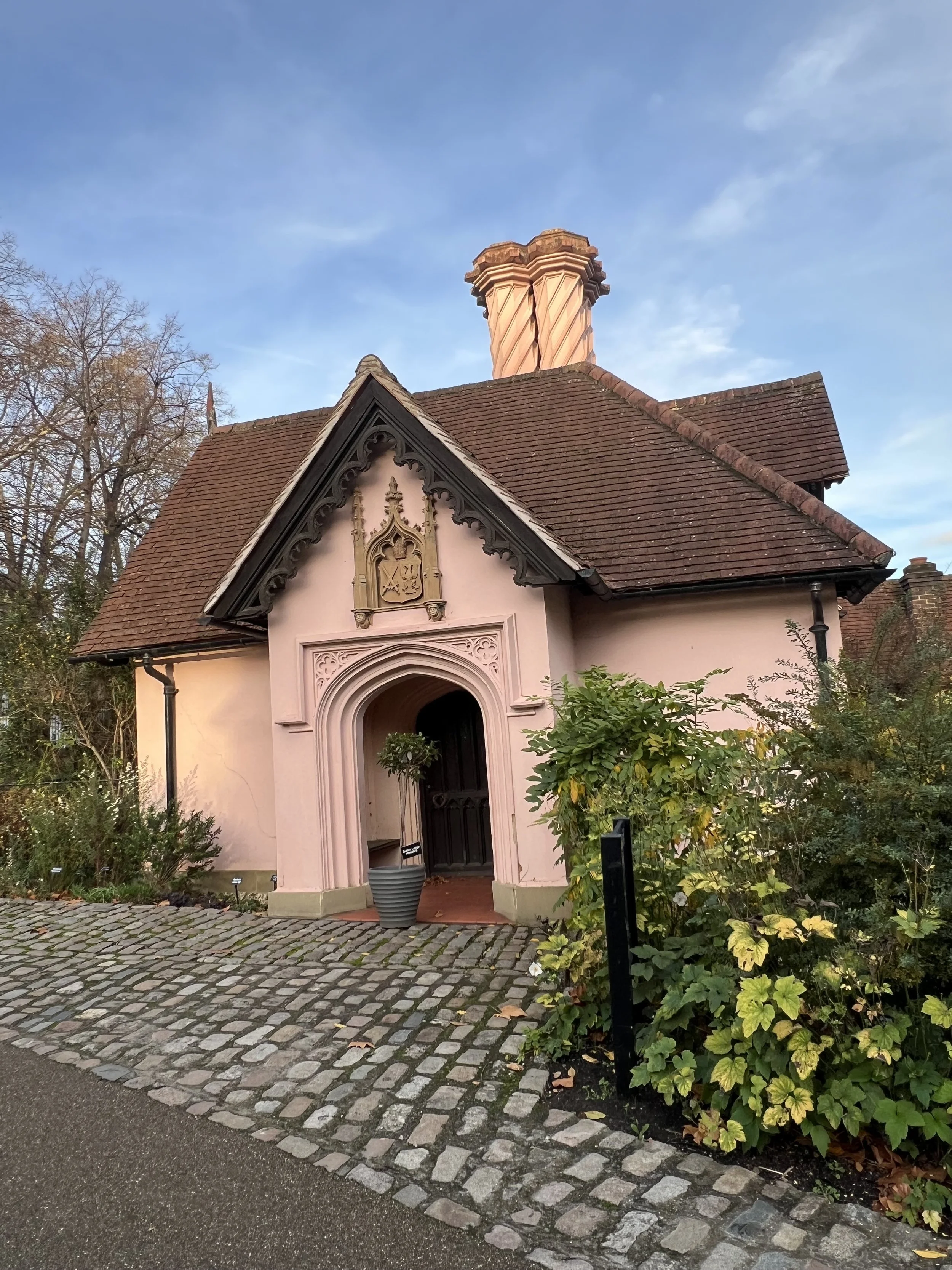 A pink cottage with cobblestones and greenery in the foreground.