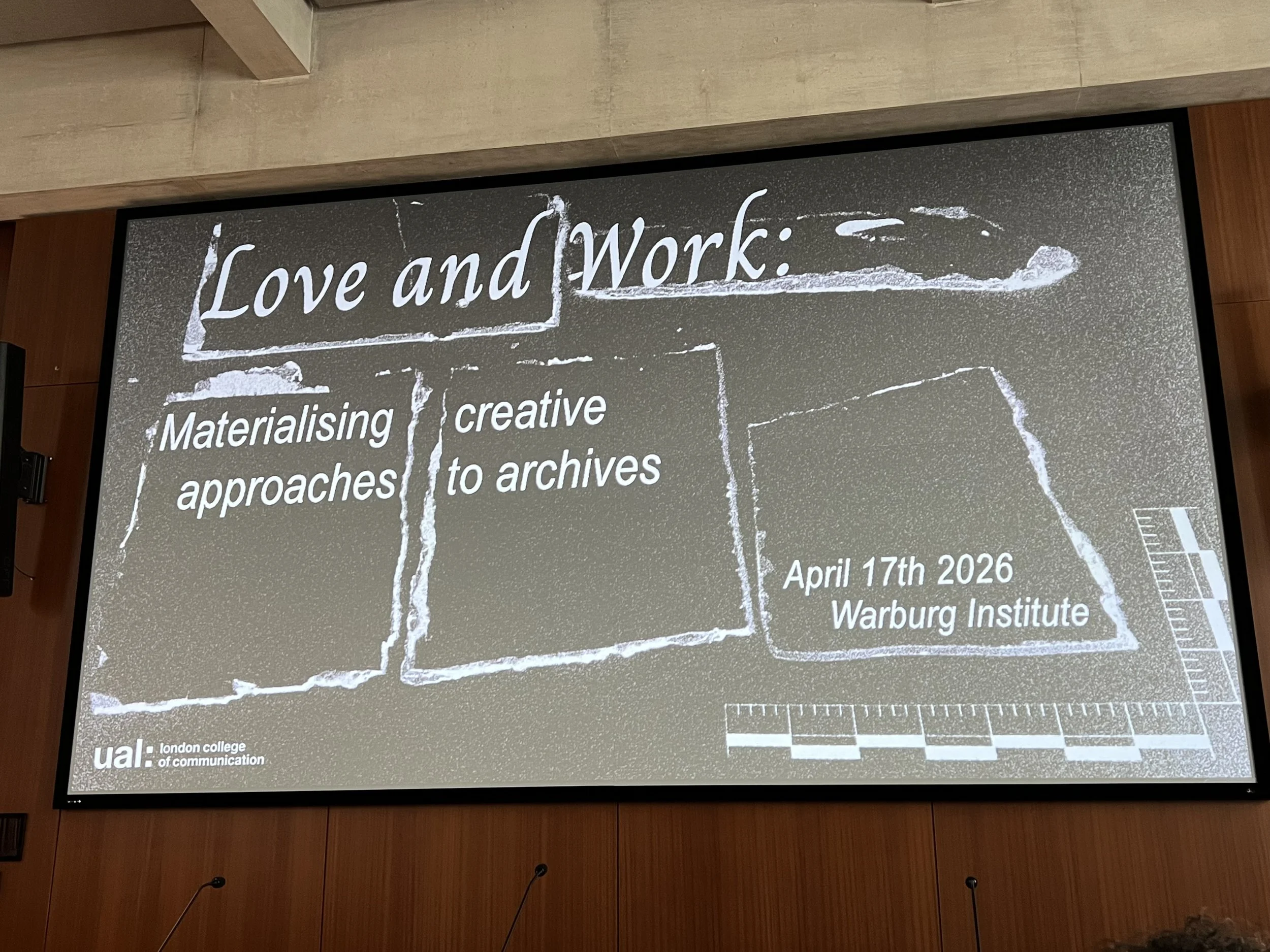 A large projector screen, showing a texturised background and the text ‘Love and Work: Materialising creative approaches’. to archives
