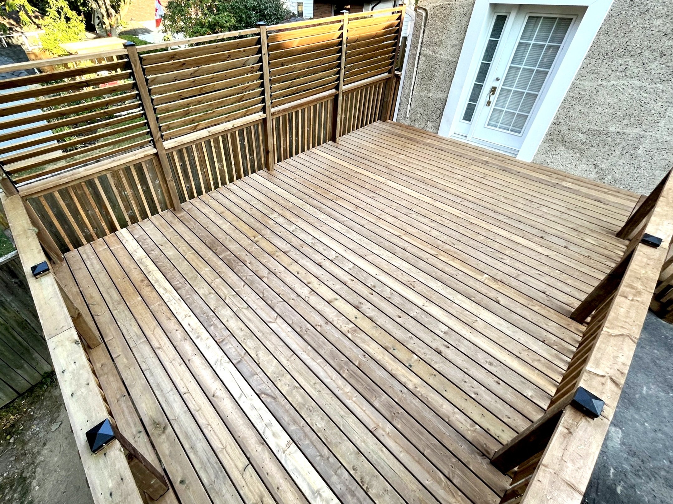 Image of a recently built wooden deck with a privacy lattice fence, attached to a house with white-framed glass door, in a backyard setting.