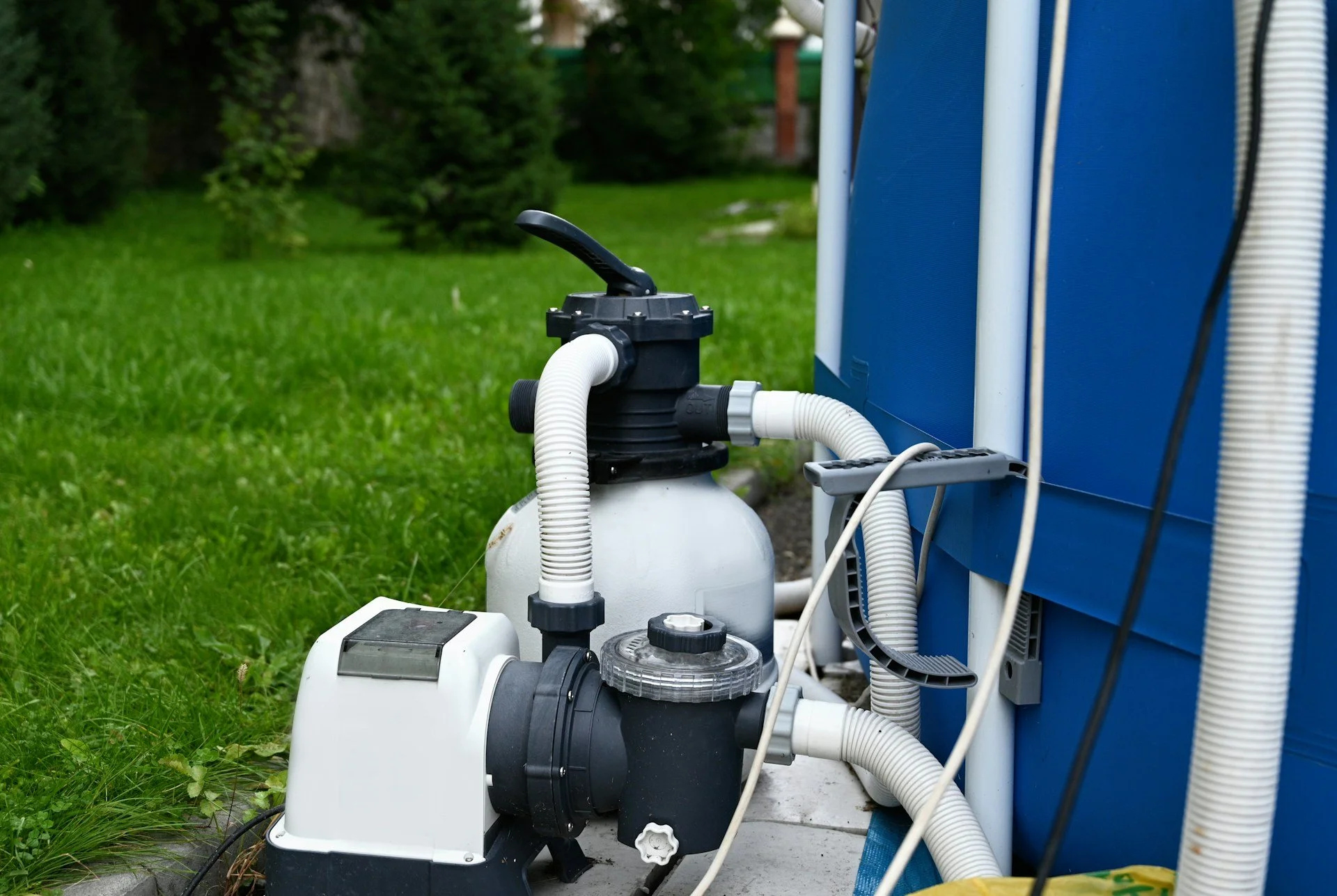 In-ground swimming pool filter system with pipes and pump outdoors on grass.