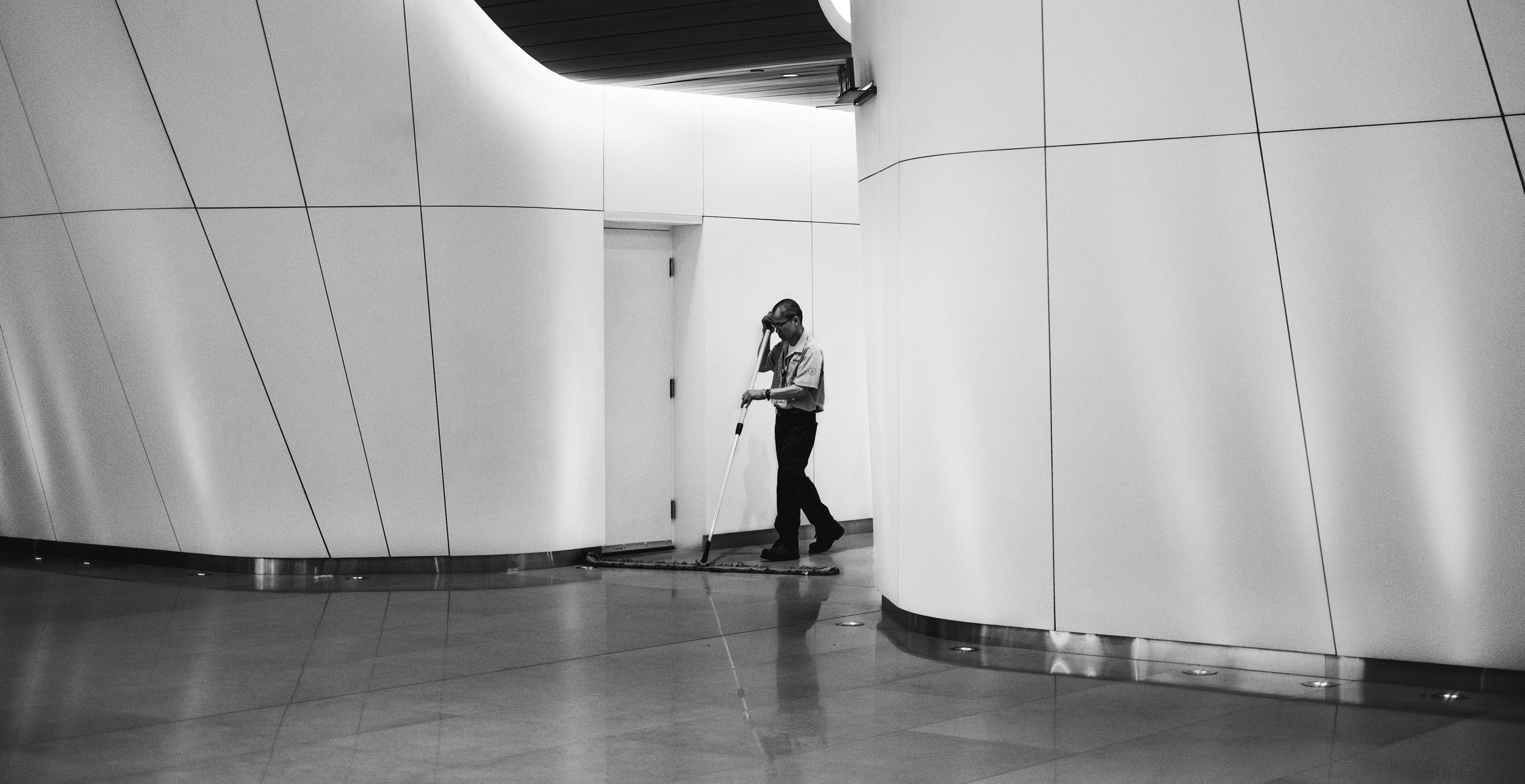 A person in uniform mops the floor of a modern, minimalistic interior space with curved, white walls.