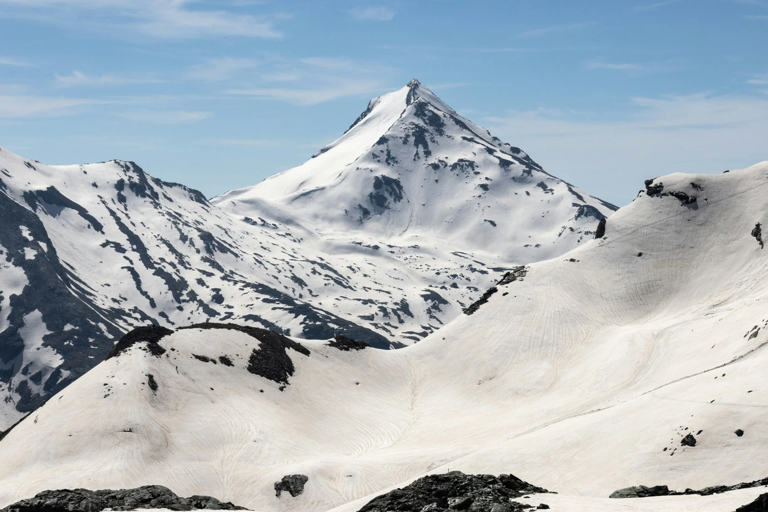 Montagnes enneigées sous un ciel partiellement nuageux avec un sommet pointu.