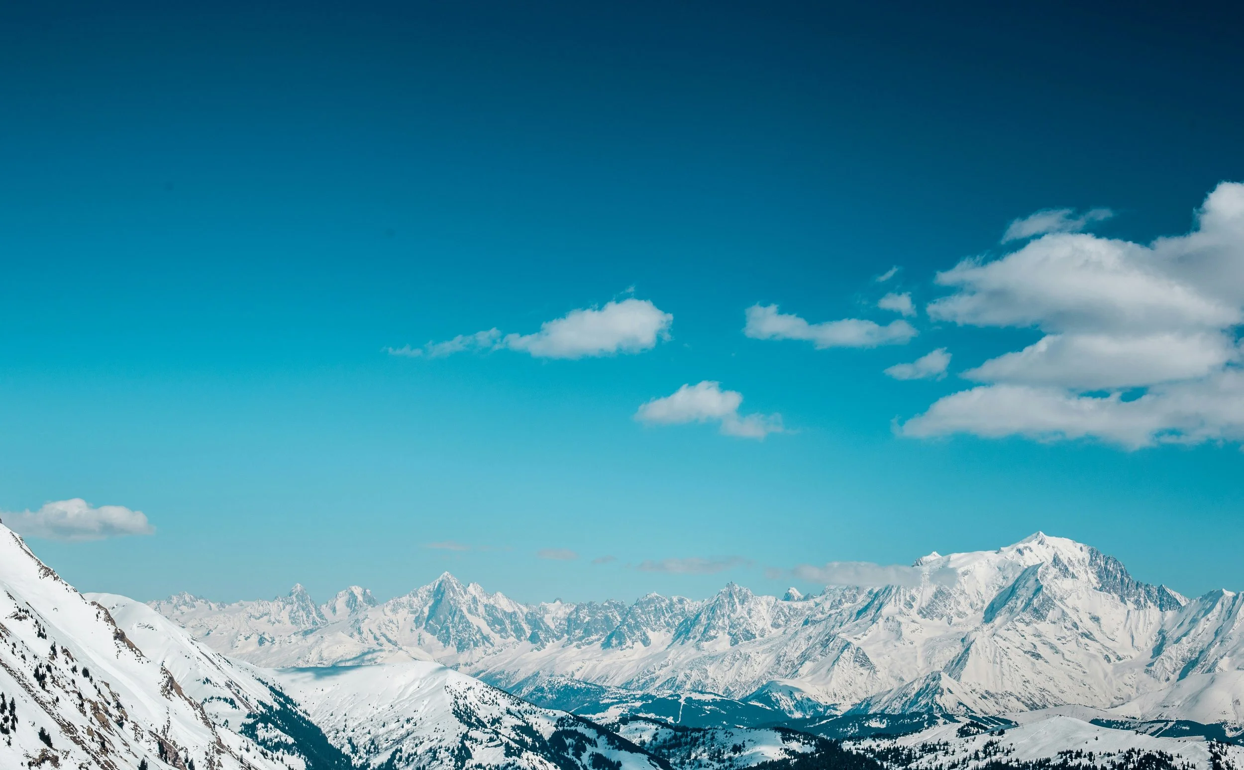 Paysage de montagnes enneigées sous un ciel bleu avec quelques nuages.