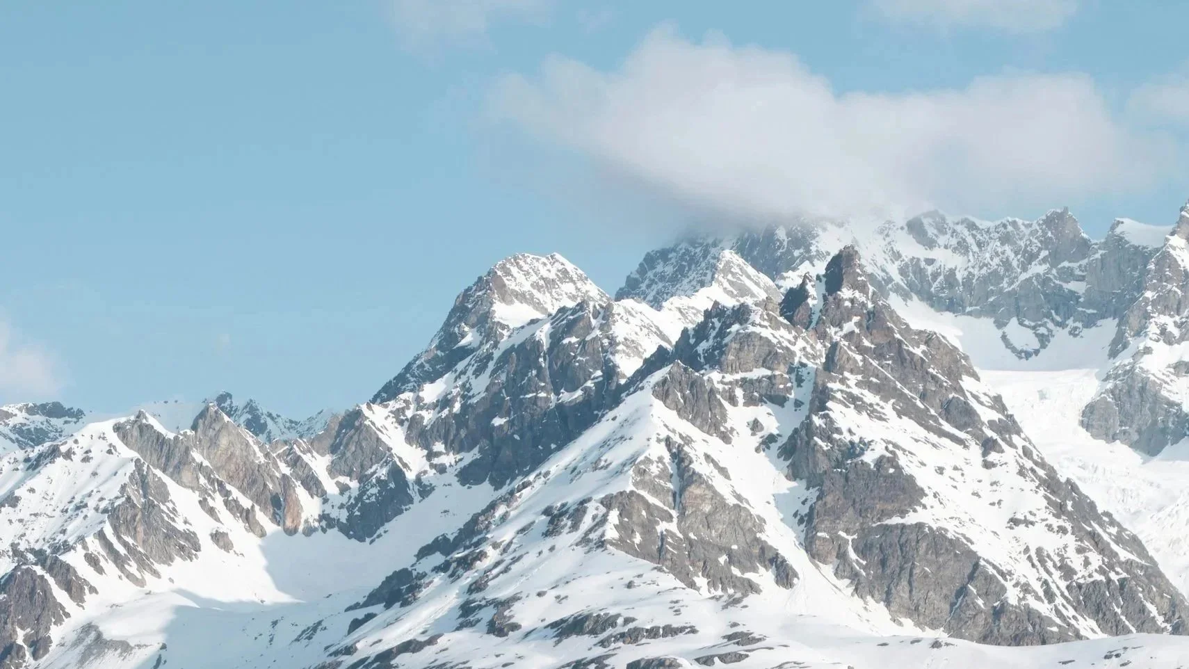 Chaîne de montagnes enneigées sous un ciel bleu avec quelques nuages.