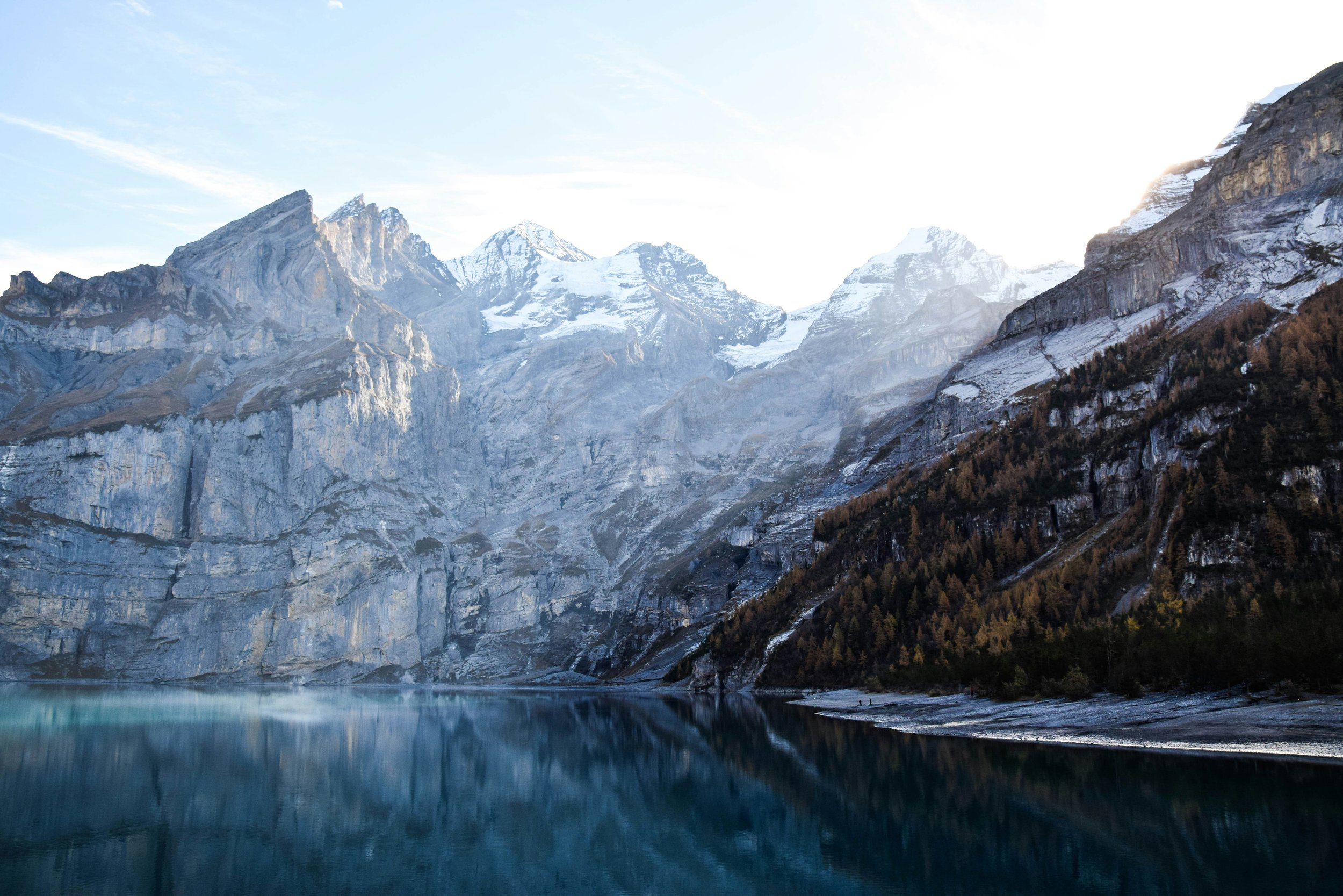 Un lac entouré de montagnes enneigées avec reflection dans l'eau, forêt au bas des montagnes, ciel clair.