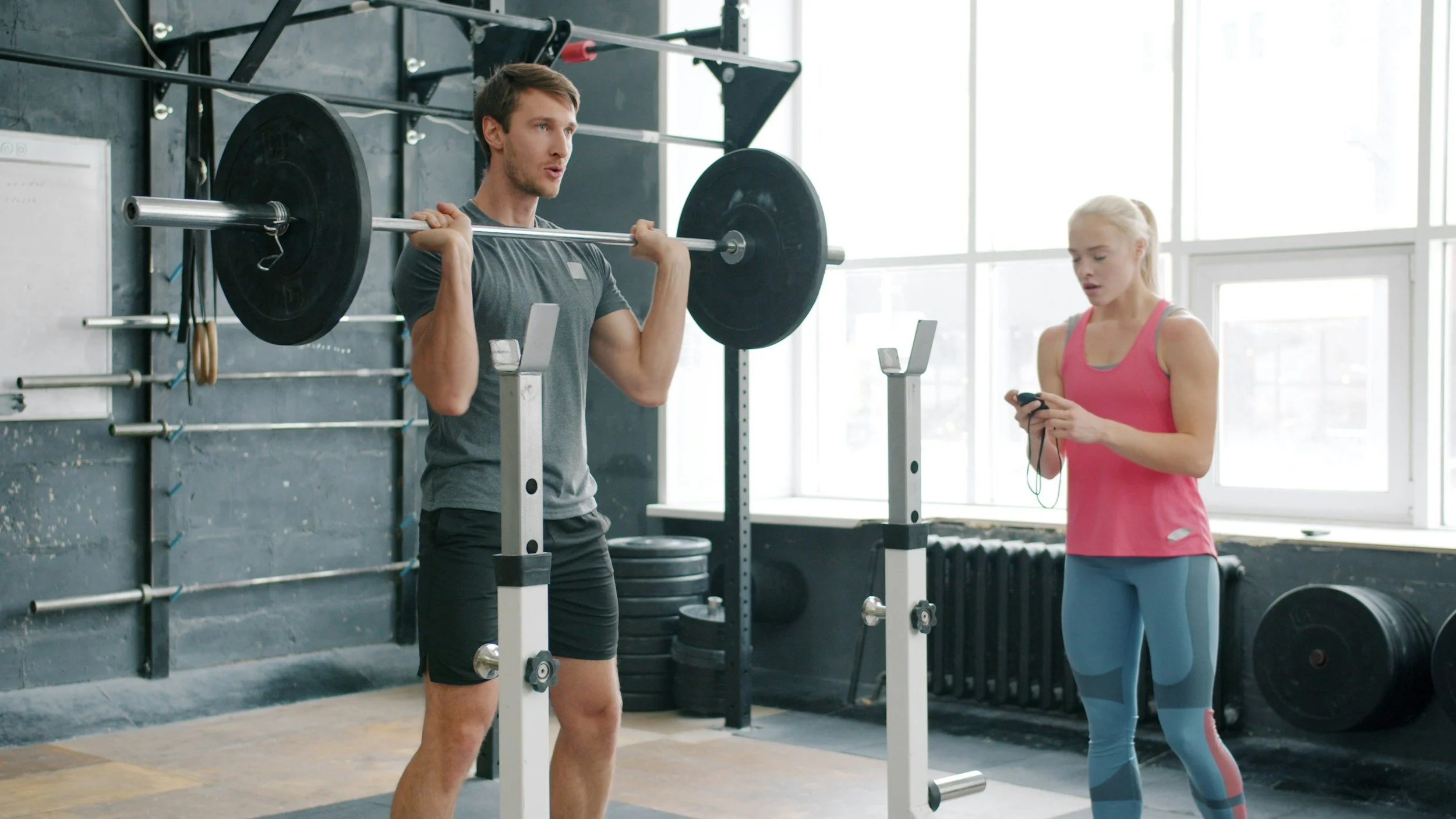 One man lifting a barbell while his trainer times him off to the side