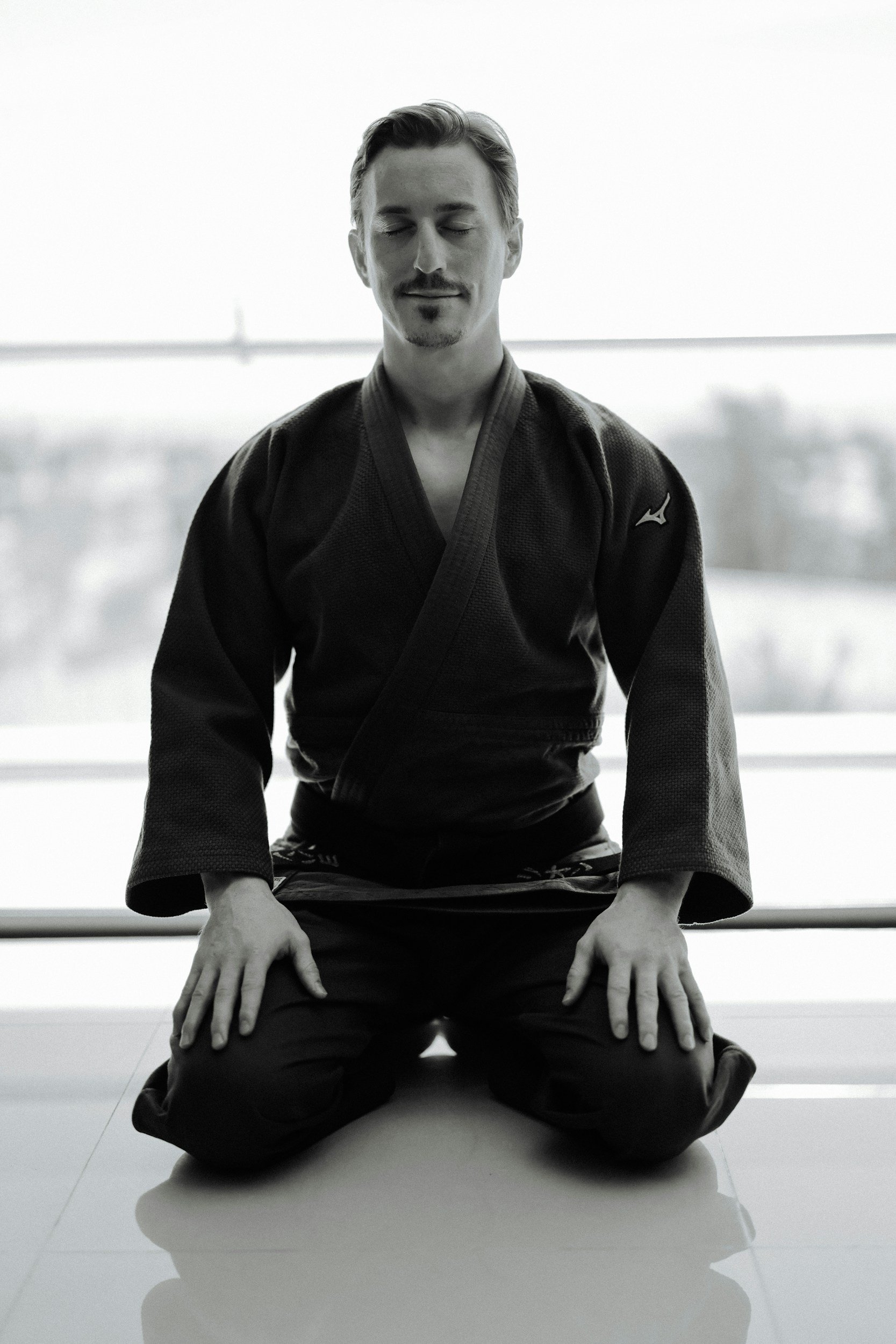 man in martial arts attire sitting on knees on floor meditating