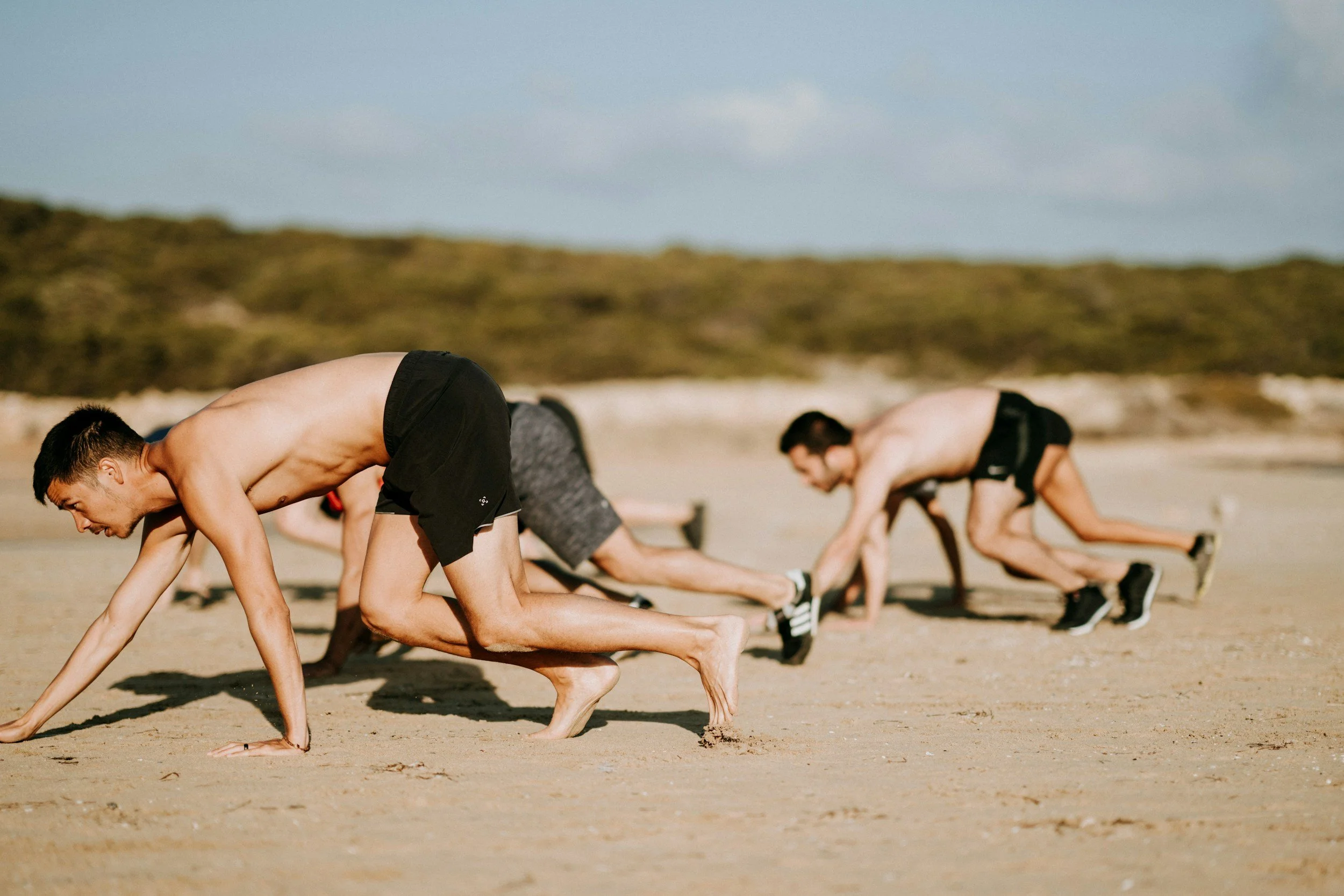 Three gentlmen performing bear crawl exercise outdoors