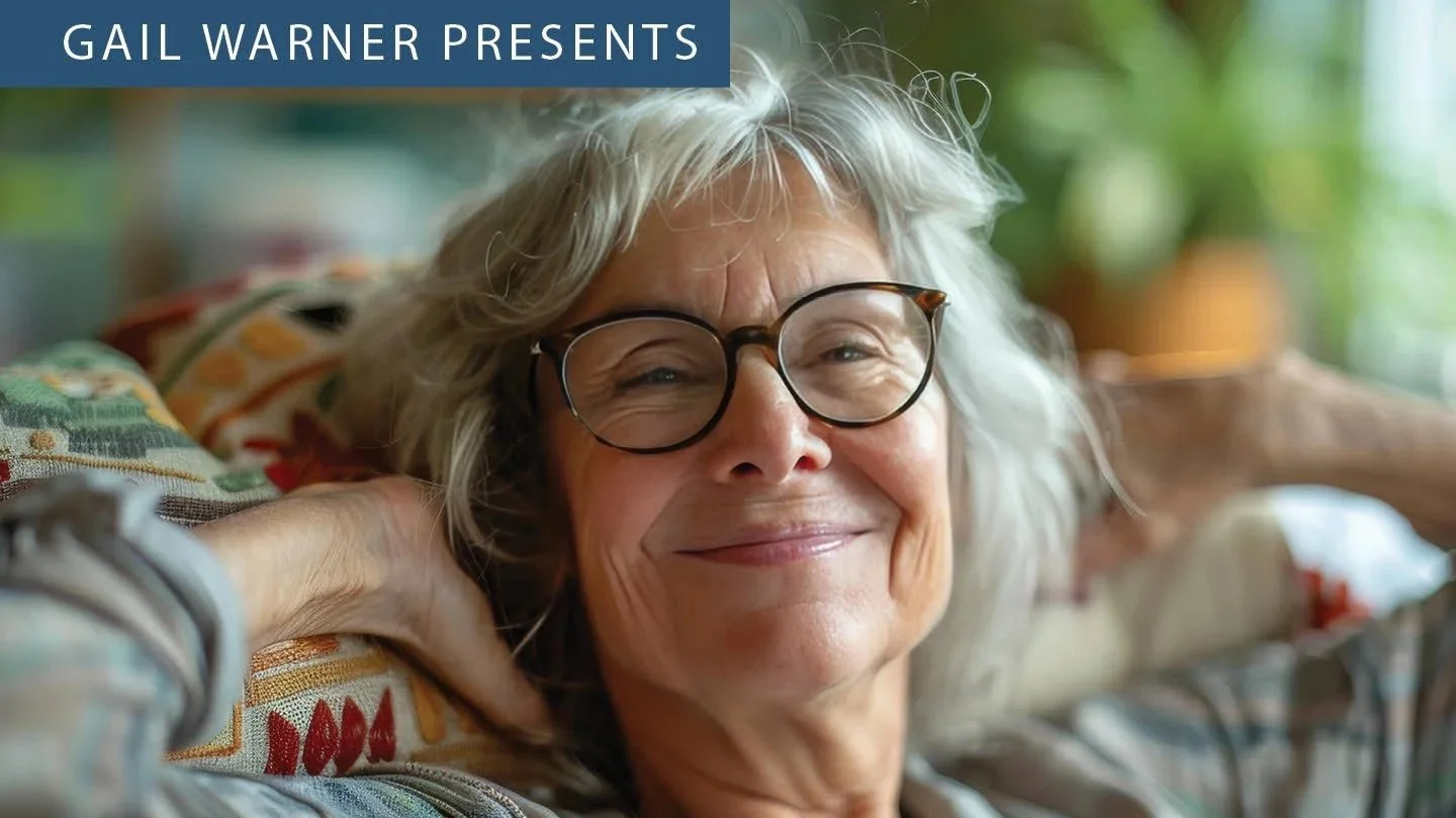 Smiling older woman with glasses relaxing on a colorful sofa in a bright room.