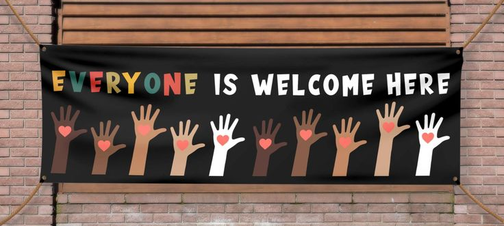 Banner with colorful text that reads 'Everyone is Welcome Here' and illustrated raised hands with hearts on palms against a brick wall background.