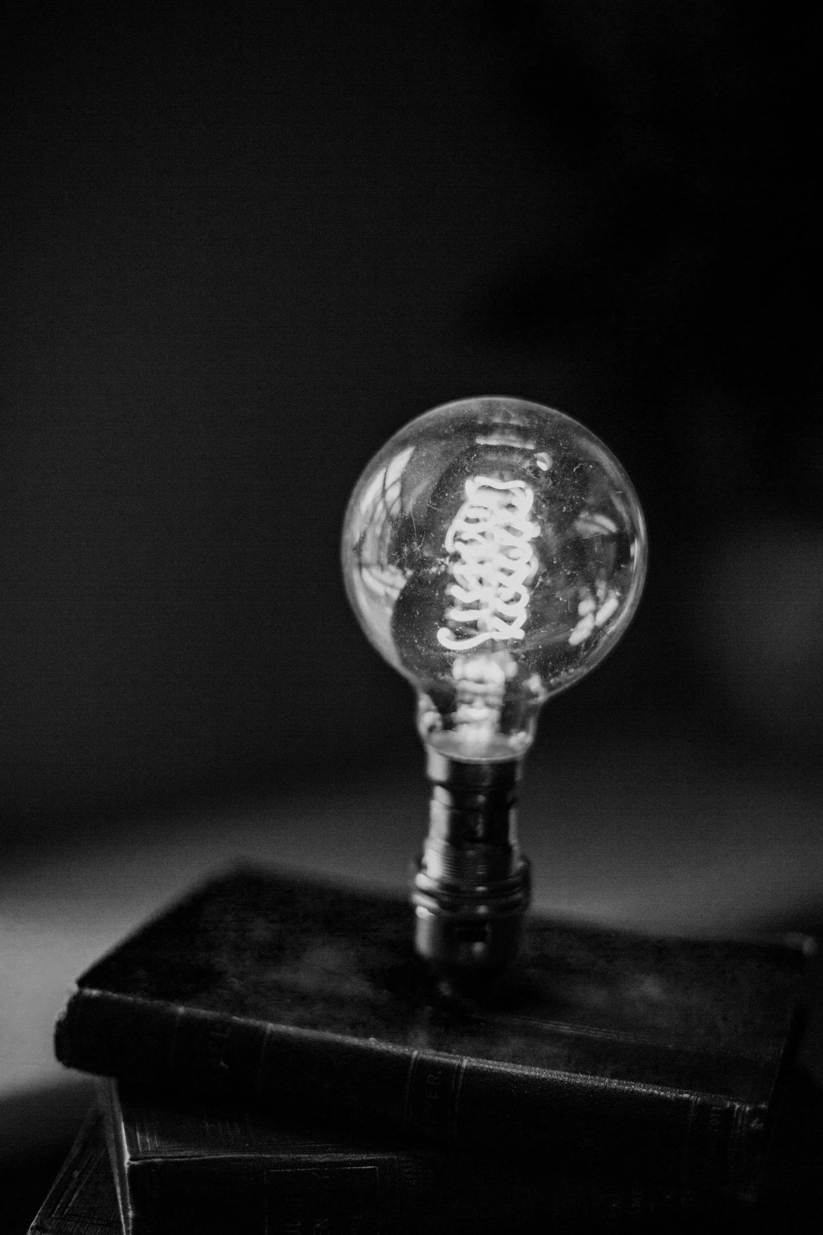 A clear incandescent light bulb placed on a black book, with a dark background.