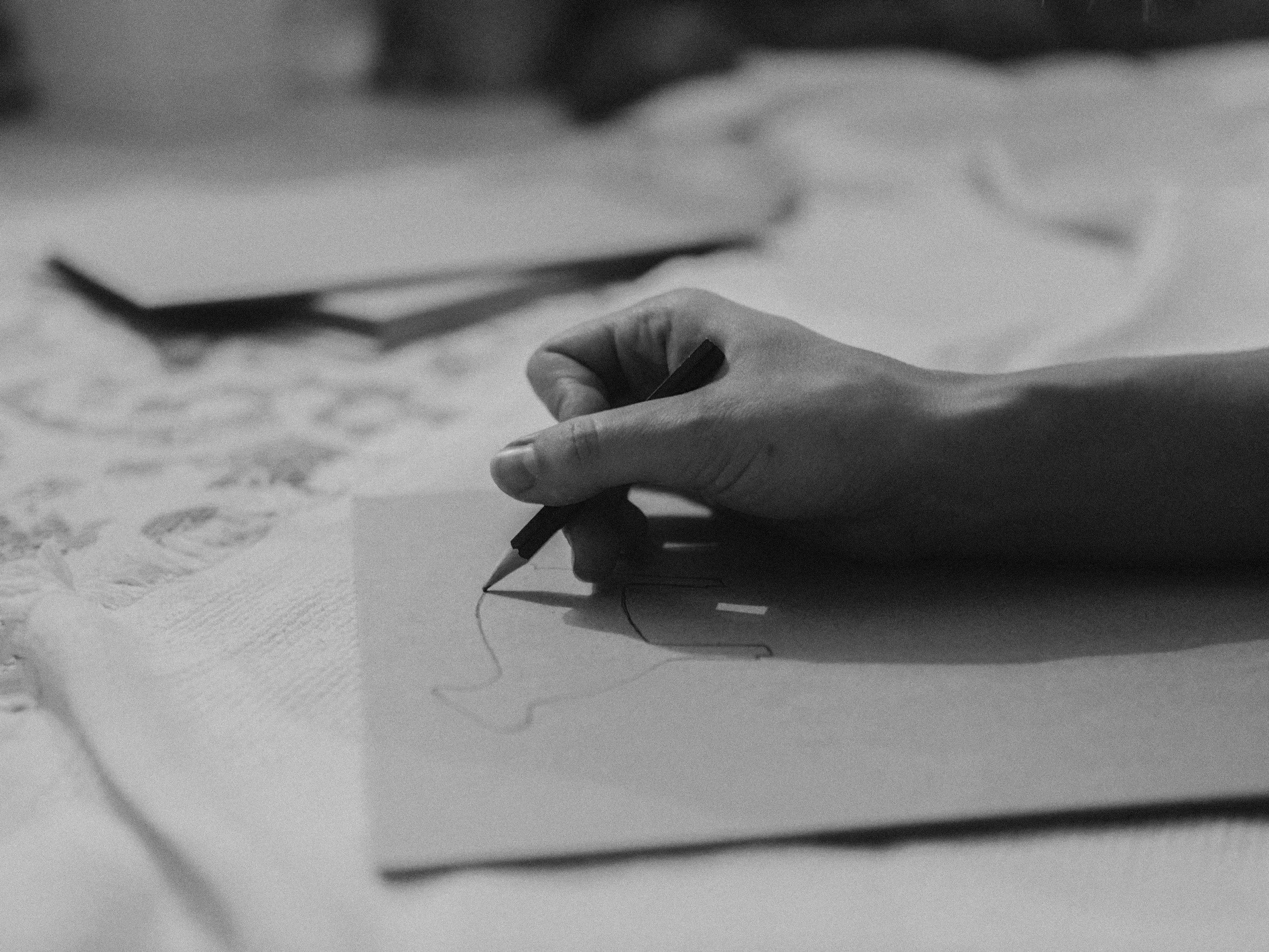 Close-up of a person’s hand holding a pencil, drawing on paper with scattered sketches and diagrams.